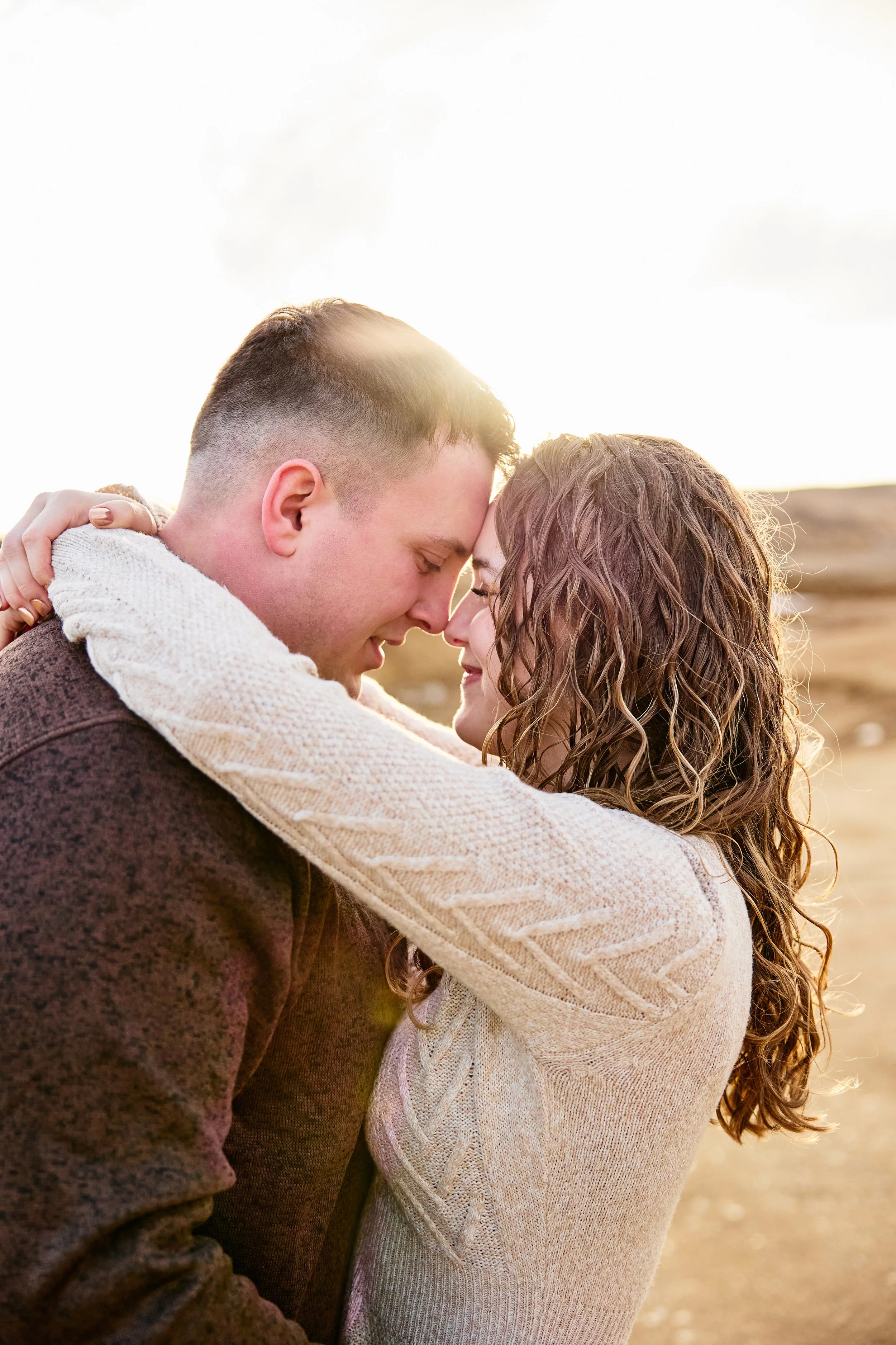 A couple with closed eyes smiling and touching foreheads outdoors during sunset
