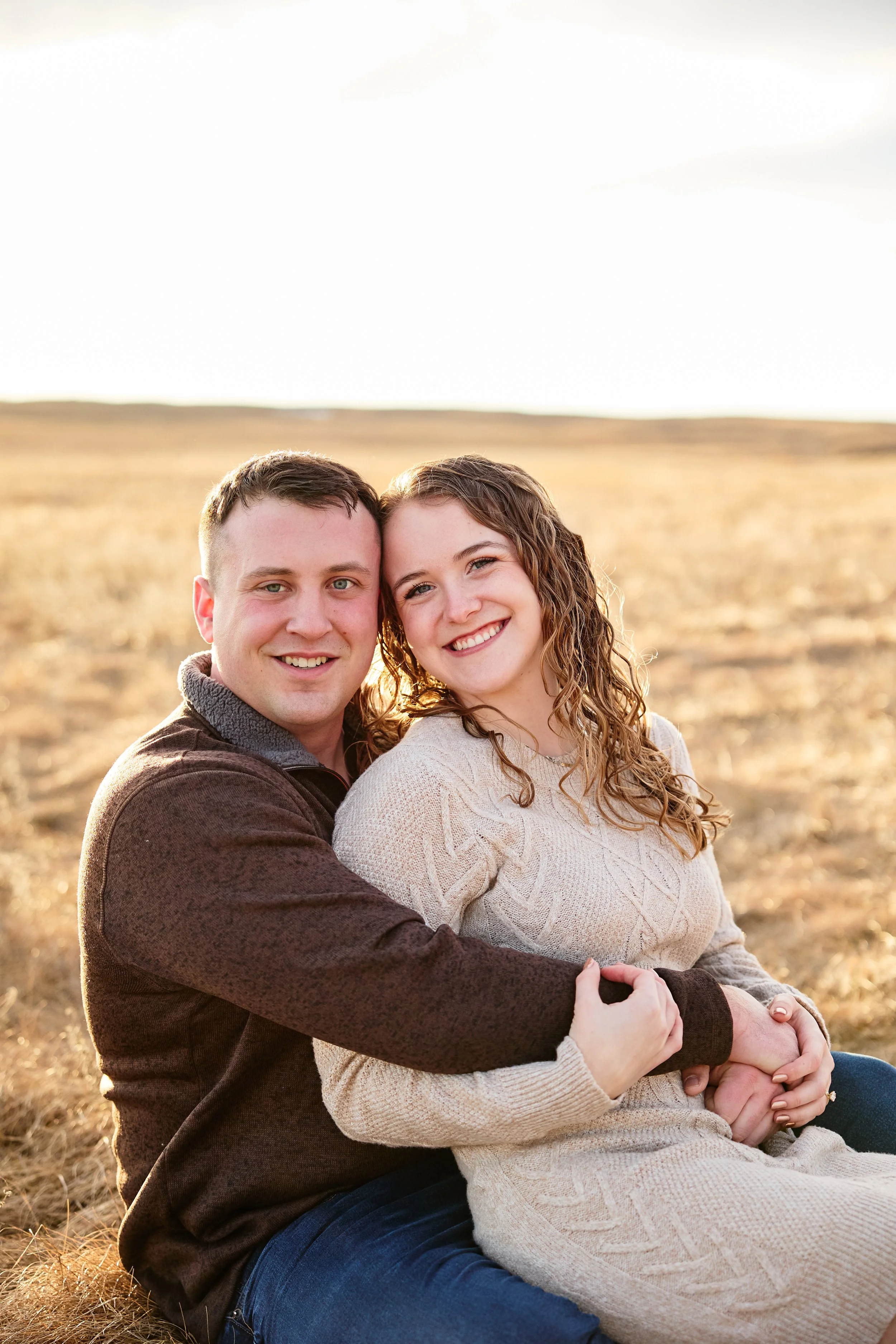 A happy couple sitting together outdoors on a grassy field during sunset.