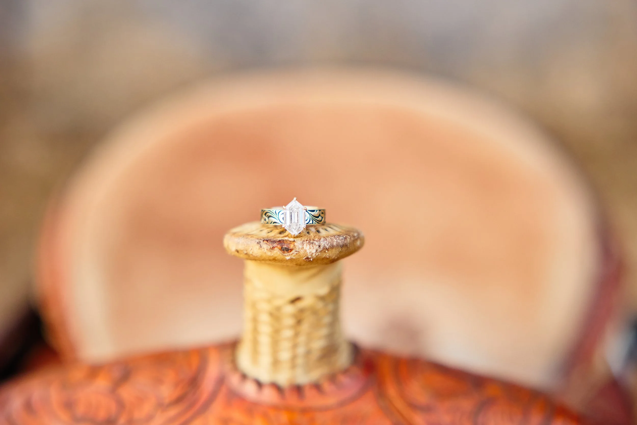 Close-up of an emerald-cut diamond ring resting on a small, textured spool-like object, with a blurred background.