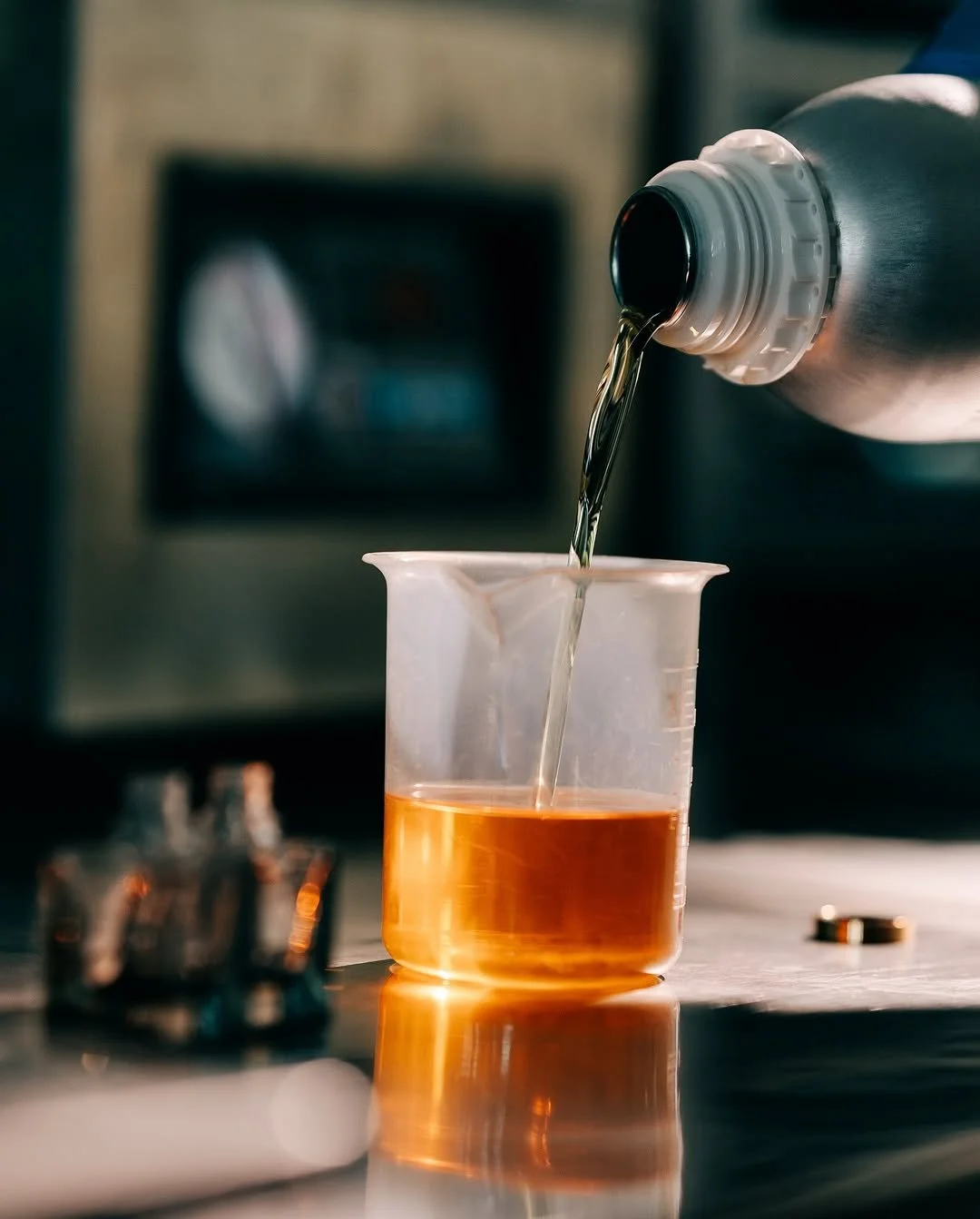 A beaker with orange liquid being filled with a liquid from a bottle in a kitchen or laboratory setting.
