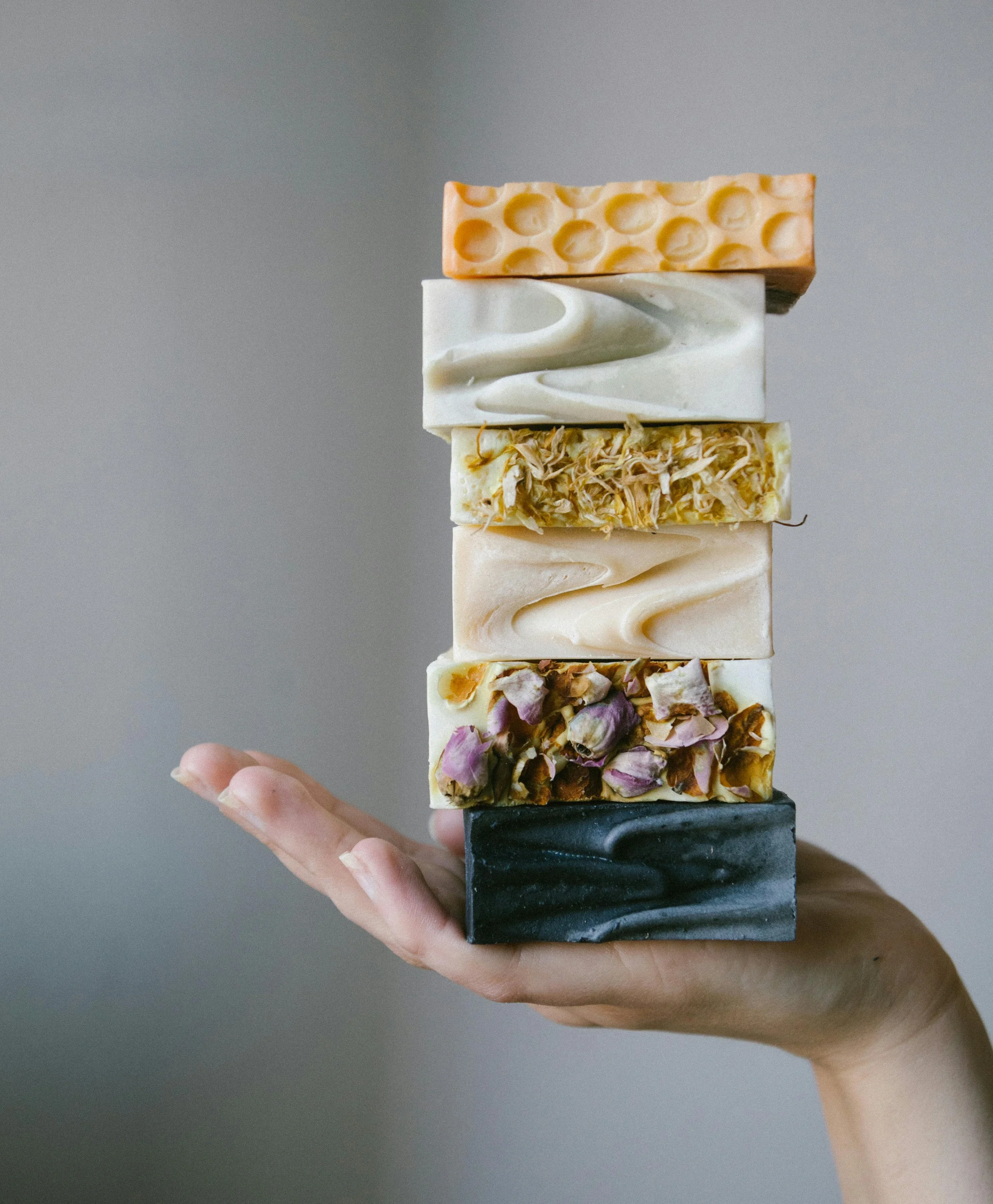 A person's hand holding a stack of five soap bars, each with different colors and textures.