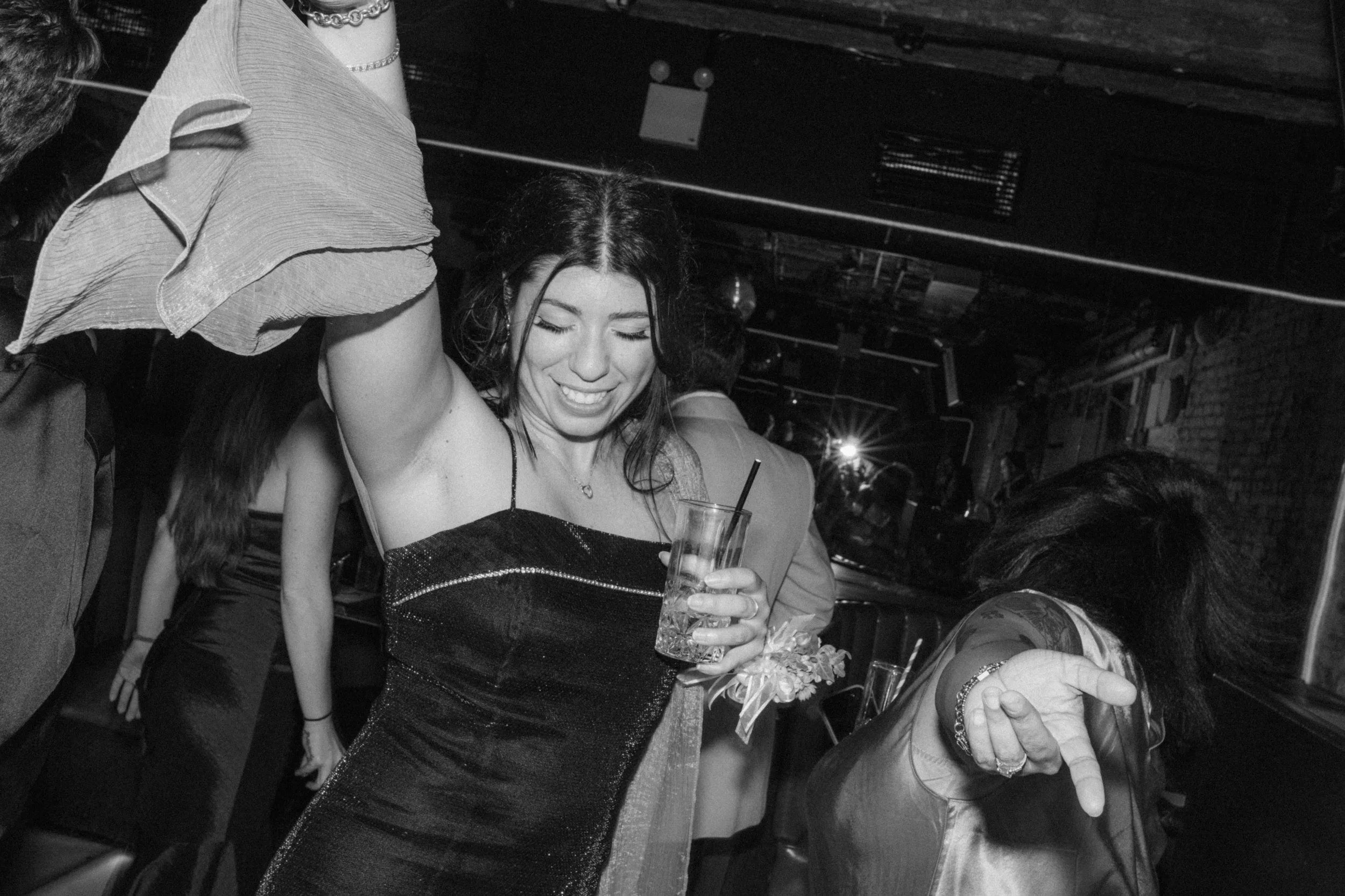A woman dancing at a party, holding a drink, and a second woman making a peace sign with her left hand.