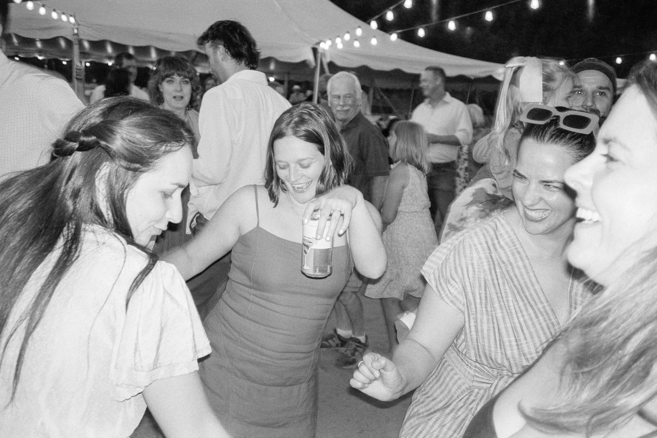 Group of people dancing at an outdoor party with string lights overhead.