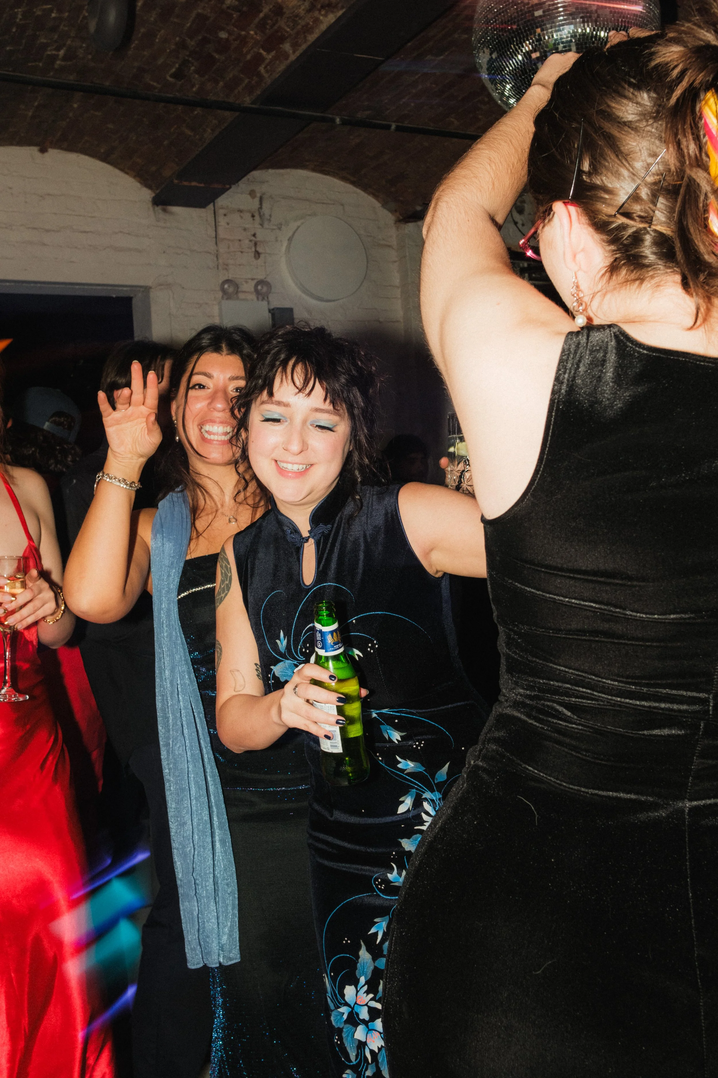 People dancing at a party, with a disco ball overhead and brick ceiling visible.