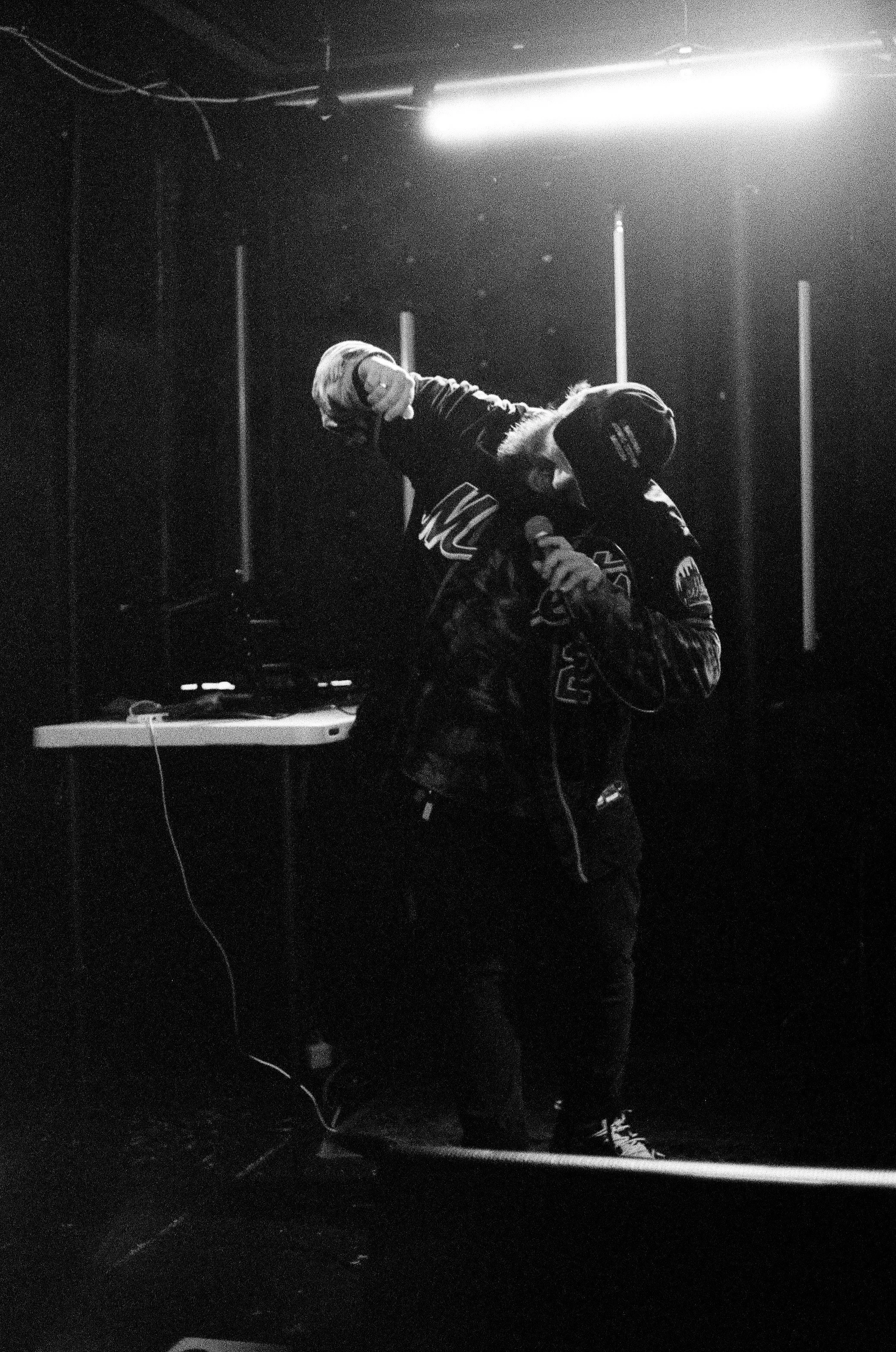 A rapper wearing a hoodie and beanie, holding a microphone.