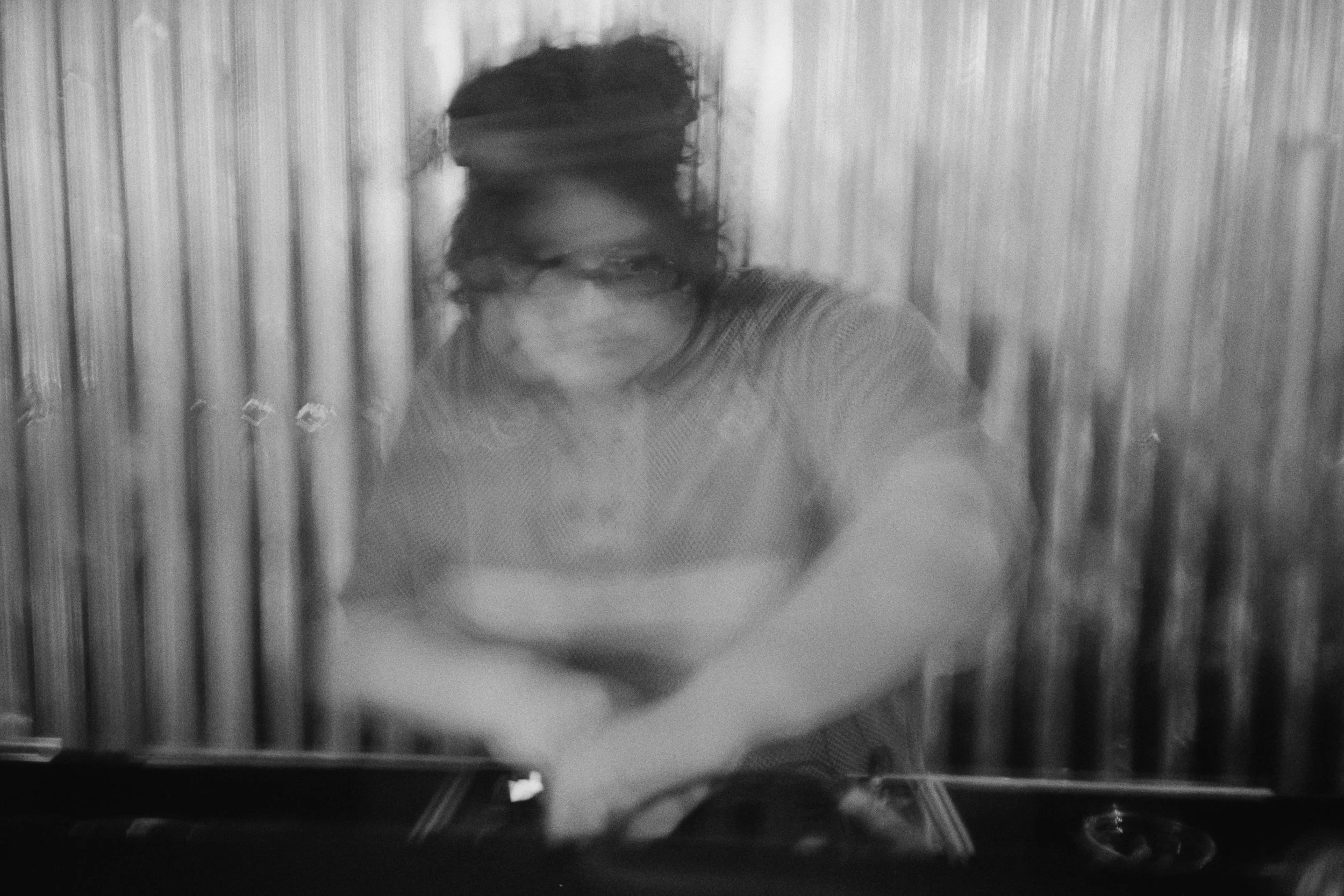 Blurry black and white image of a DJ in front of a metal wall.