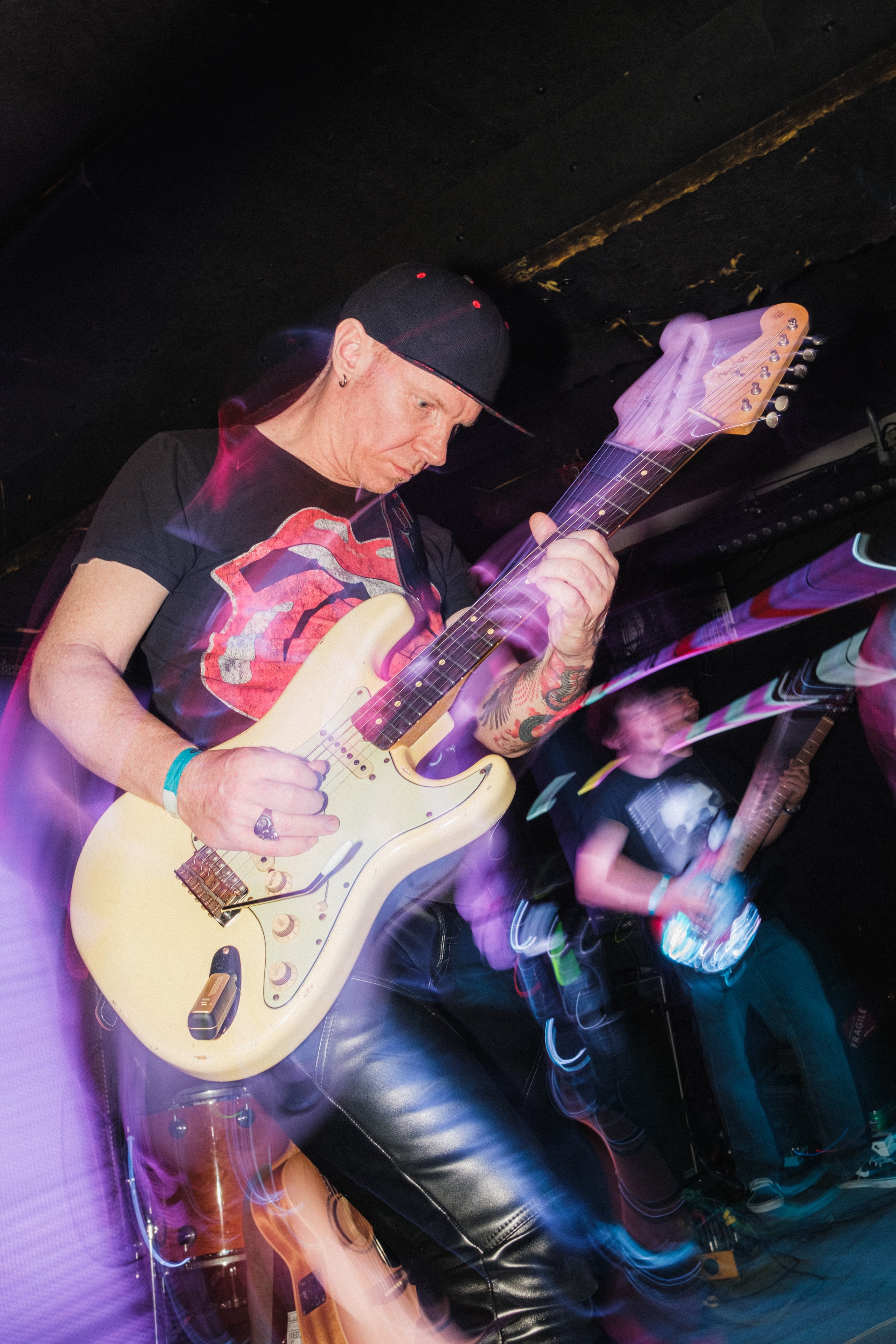 A man playing an electric guitar on stage with colorful lights and motion blur.