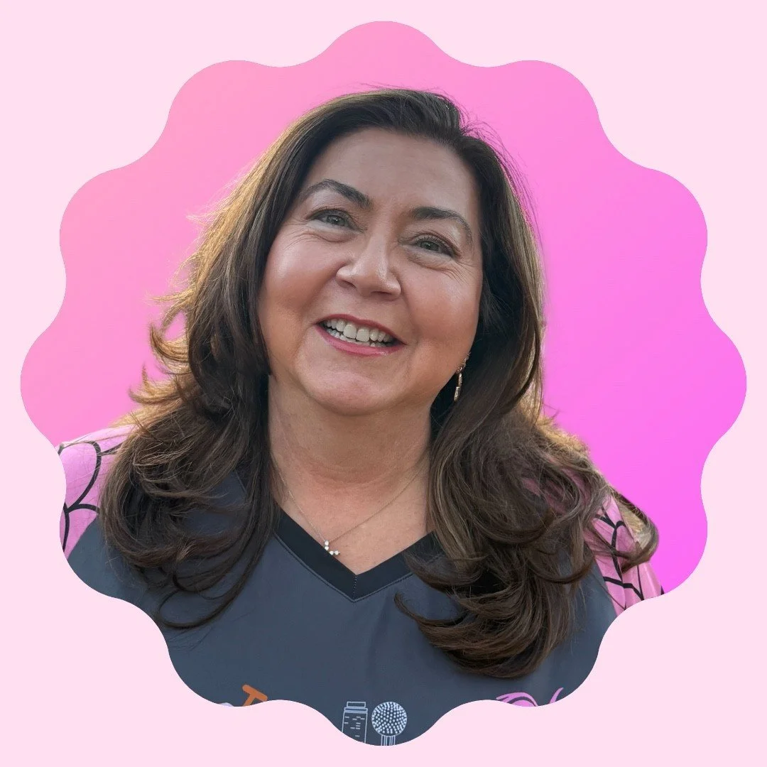 A smiling woman with brown hair wearing sunglasses on her head and a sports jersey against a pink background.