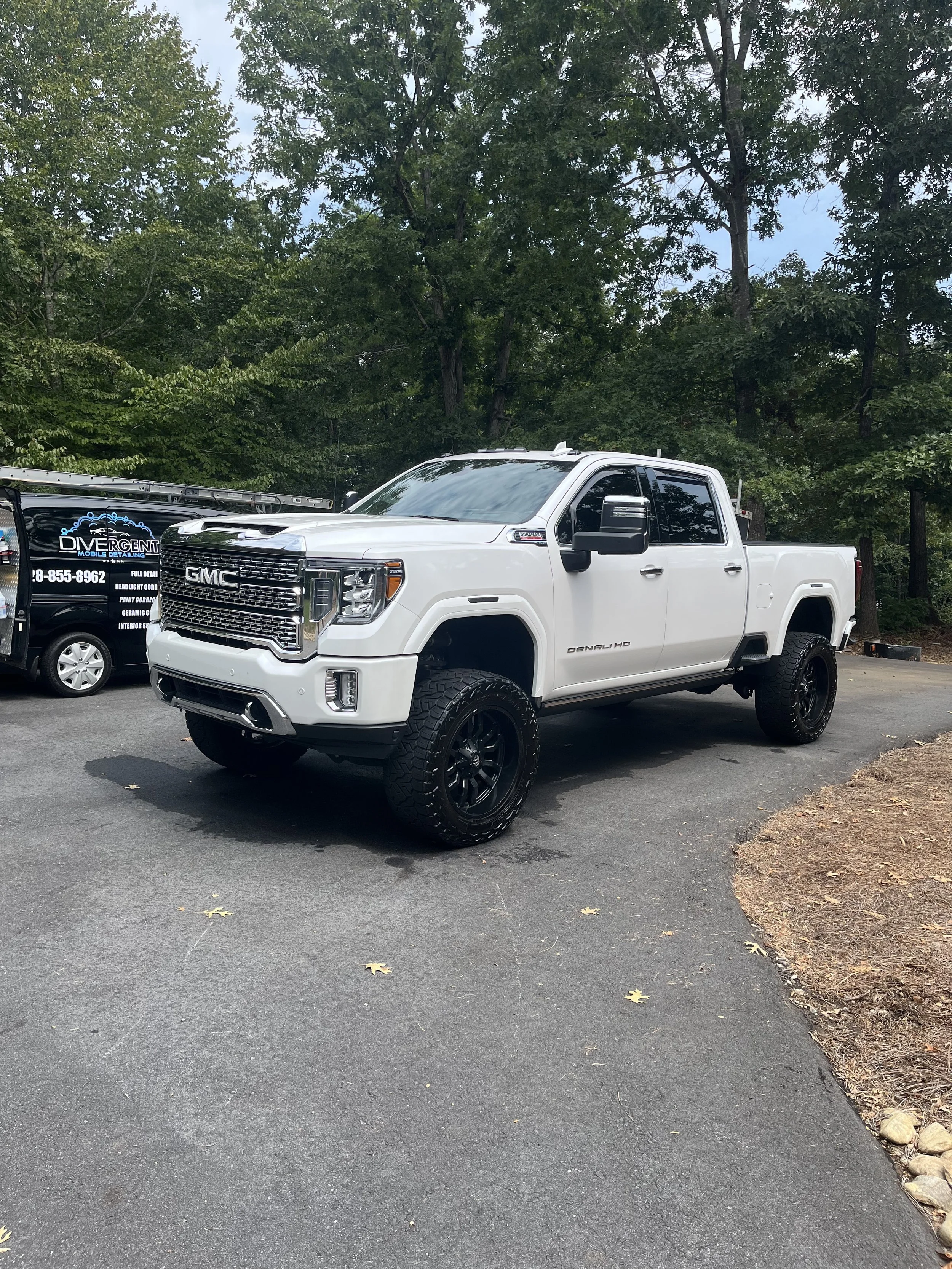 A white GMC pickup truck with black wheels parked on a paved lot near trees.