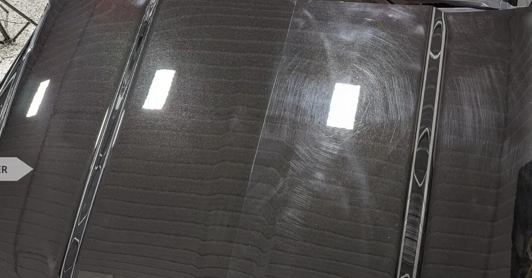 Close-up of a black, polished car surface with visible swirl marks and reflections of overhead lights.