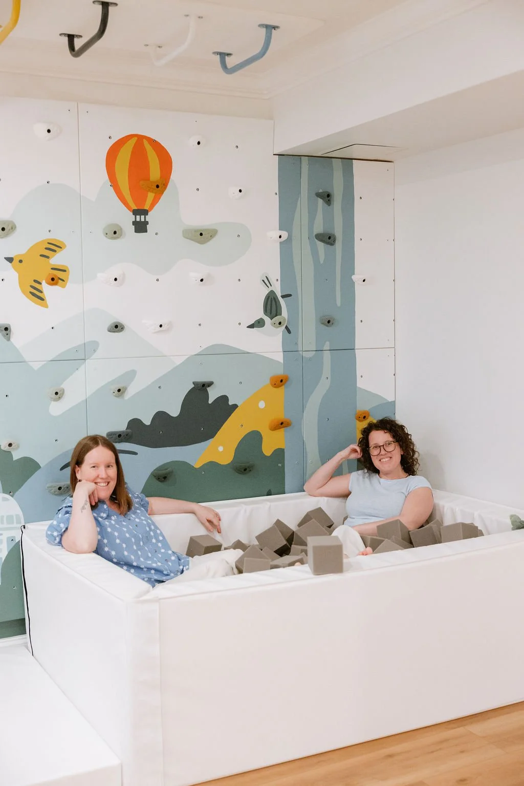 Playroom designers Kayla and Kristin siting in a foam pit in front of customised rock wall. 