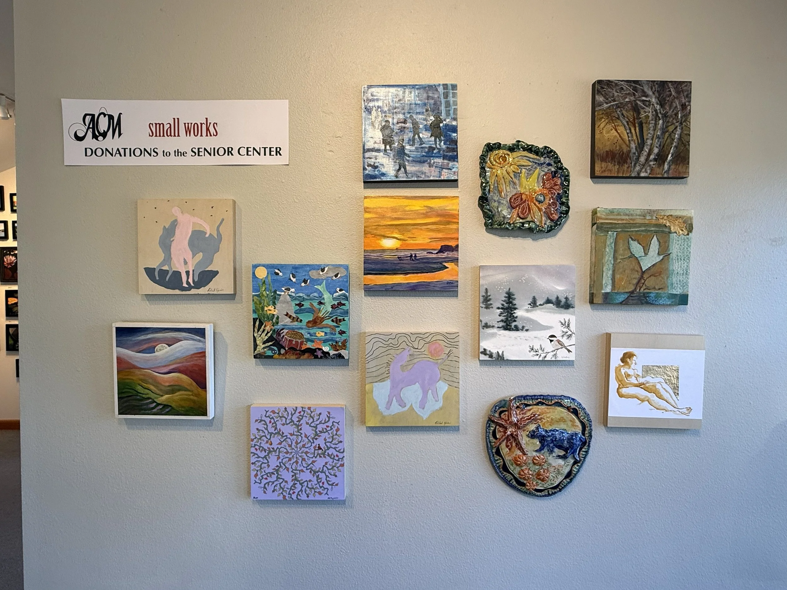 Small Works of art on a wall with a sign for donations to the senior center