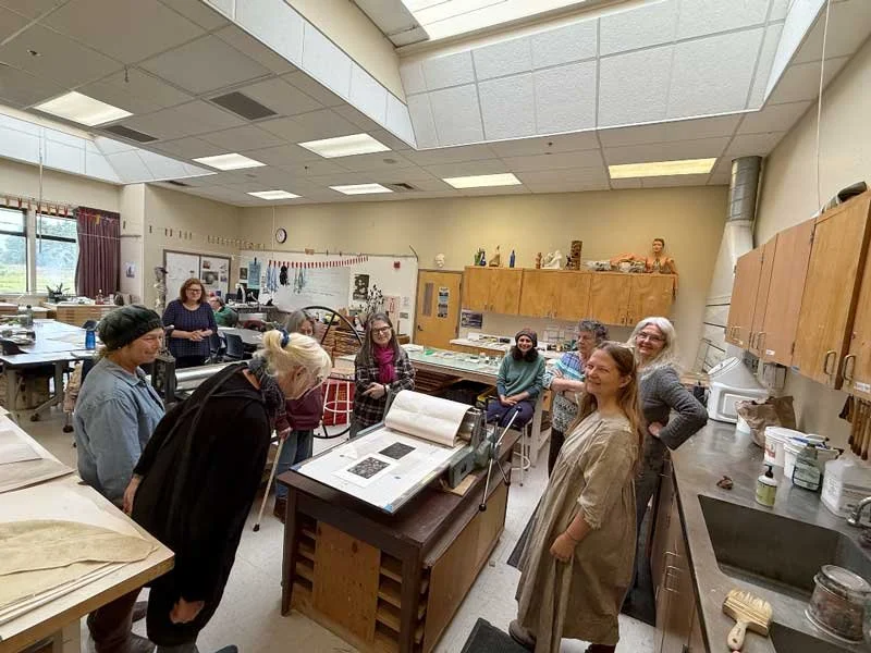 group of students in an art classroom gathered around  monoprint equipment