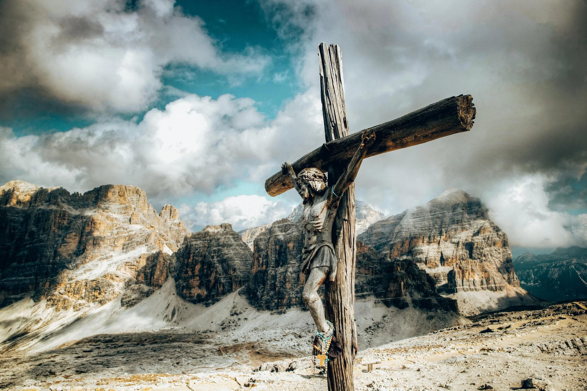 Escultura de Cristo crucificado en un paisaje montañoso con nubes dramáticas.