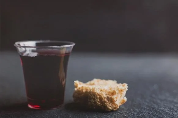 Copa de vino tinto y un pedazo de pan sobre una superficie oscura.