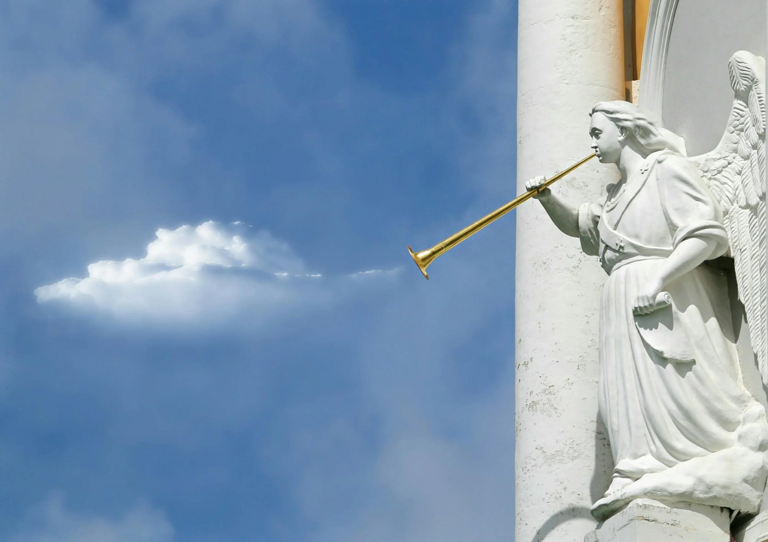 Estatua de un ángel tocando una trompeta dorada contra un cielo azul con una nube.