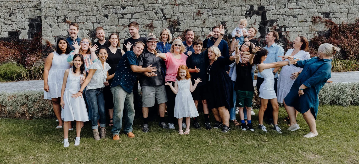 The extended family laughs together in front of a stone wall
