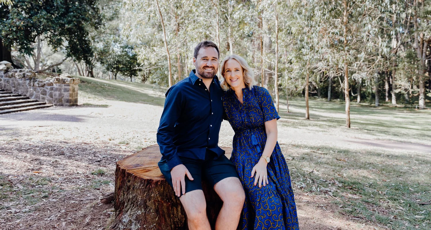 A couple sit together on a tree stump in the park