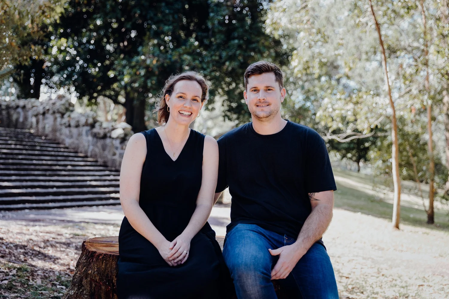A couple pose on a tree stump in front of stone steps