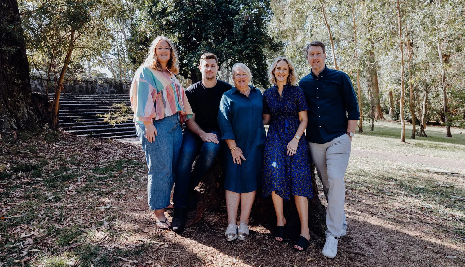 Five adults stand together under the trees