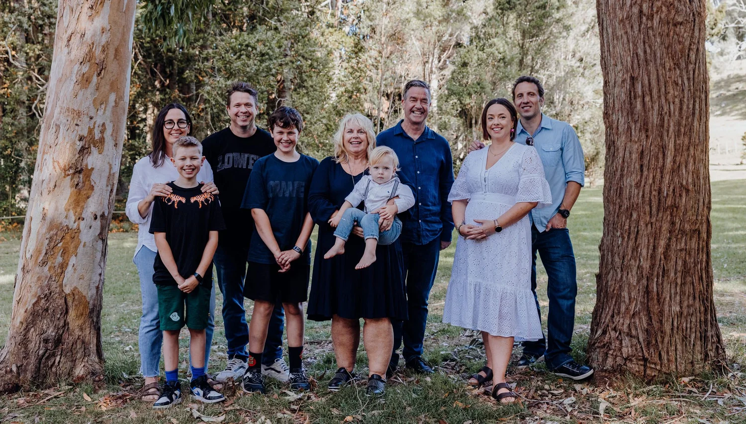 A family group stands between tall trees in the park