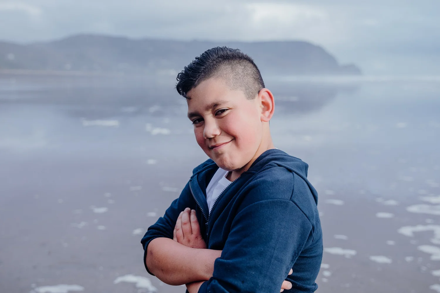 A boy with folded arms smiles on the beach