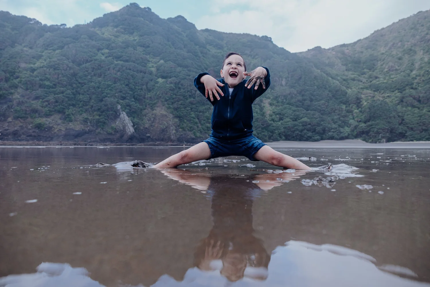 A boy pulls a funny face sitting on the wet sand