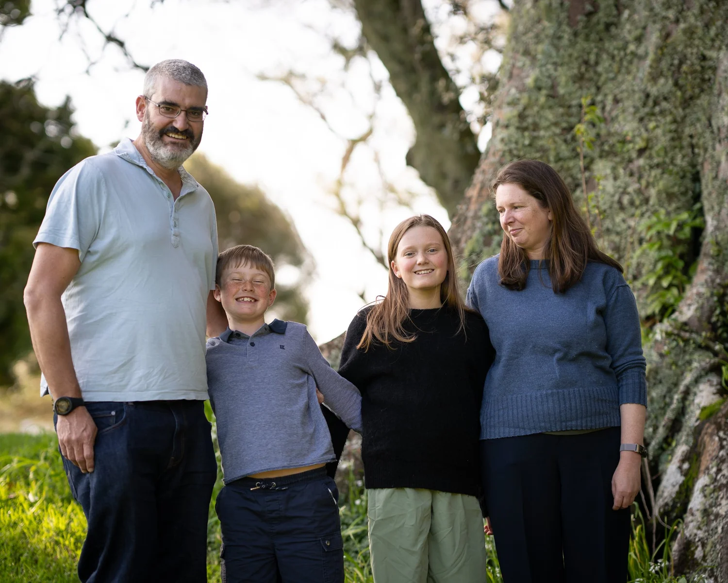 The family stands together beneath a large old tree