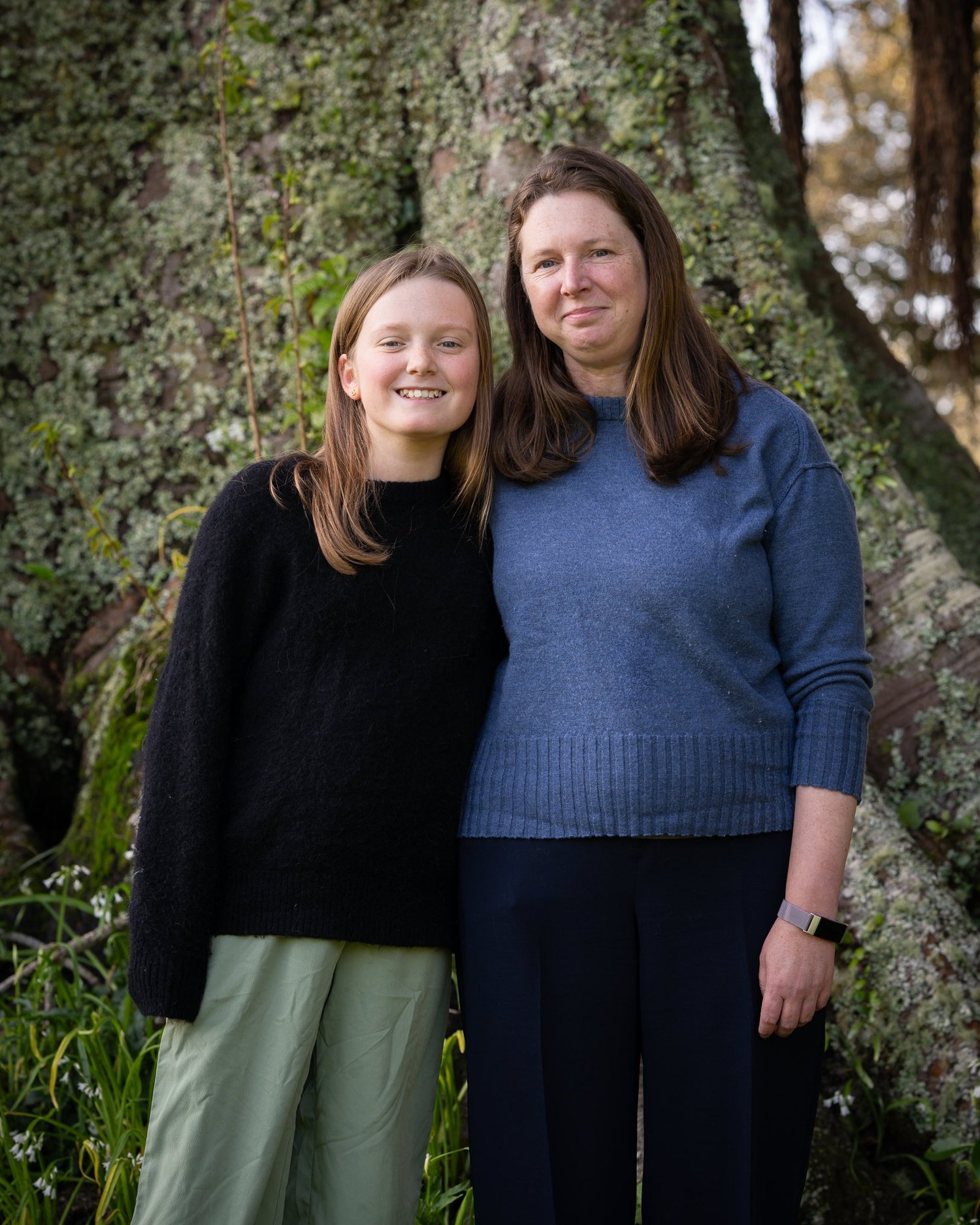 A mother and daughter stand together beneath a tree