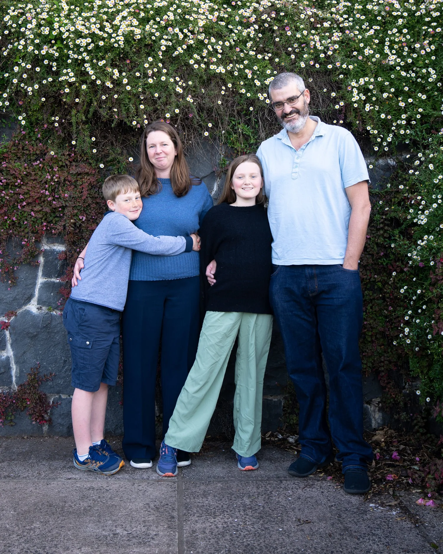 The family laughs together beside a flowering stone wall