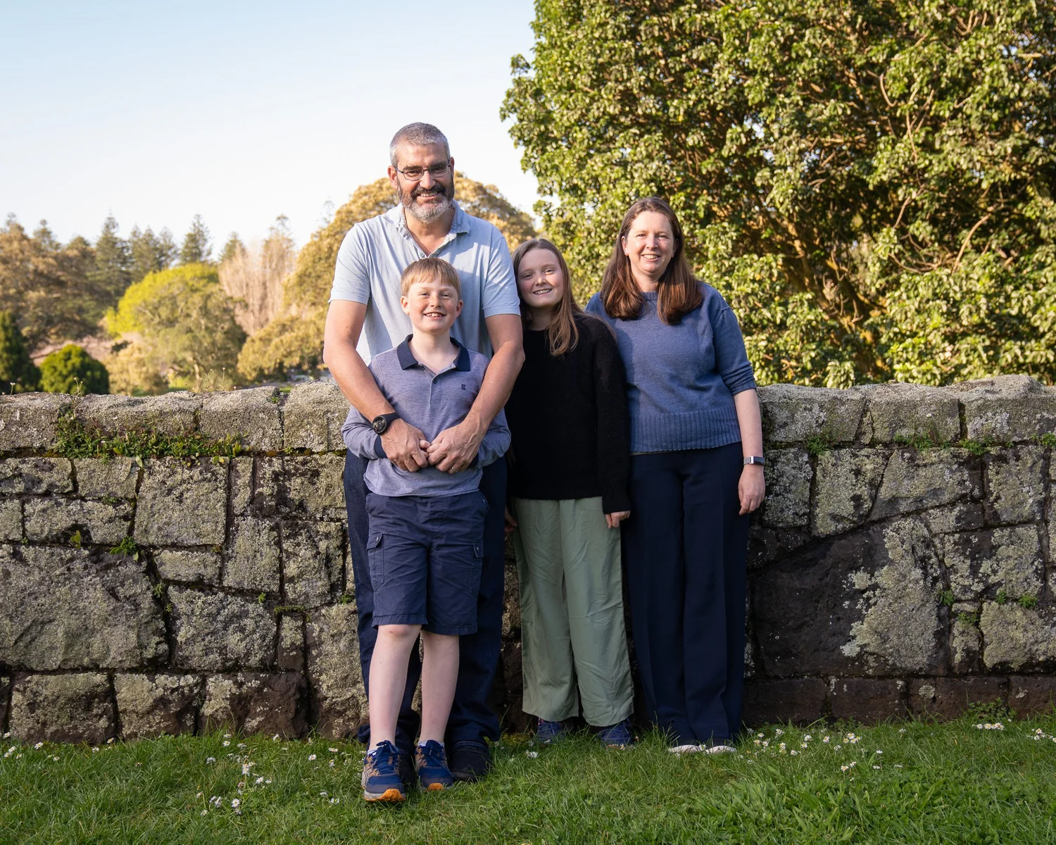 The family together beside a stone wall under autumn trees
