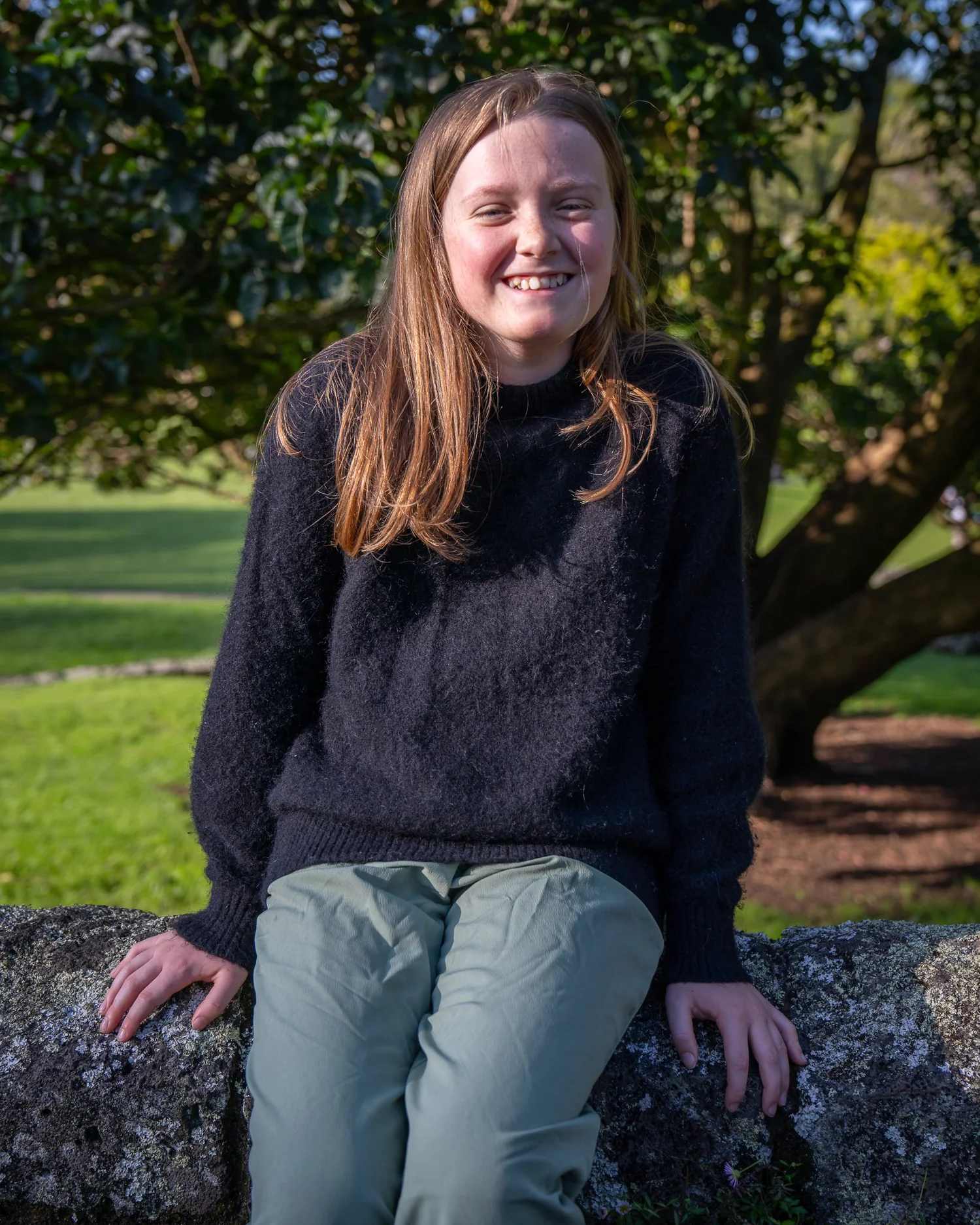 A girl sits on a rock smiling at the camera