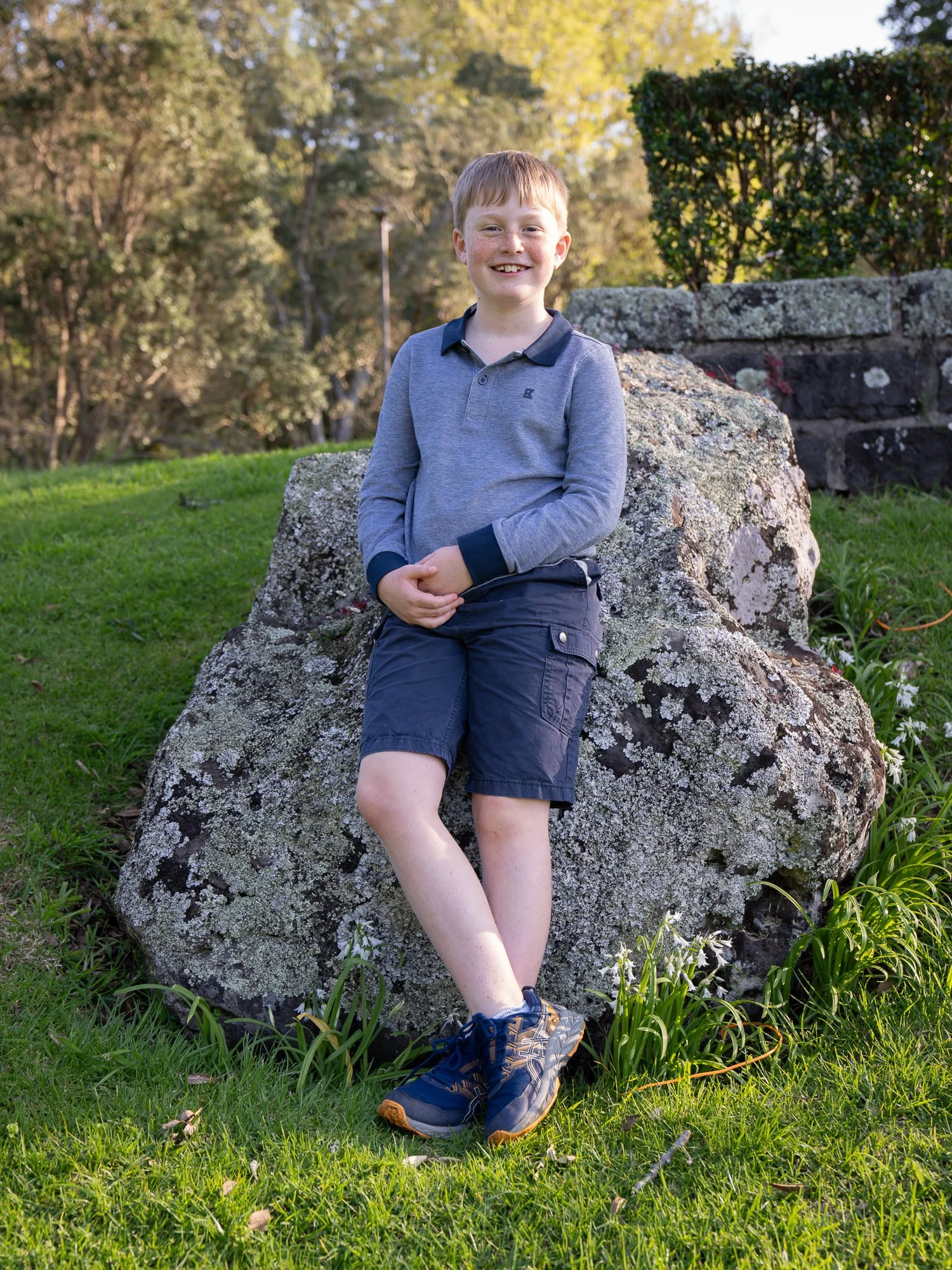 A boy sits on a large rock in the park
