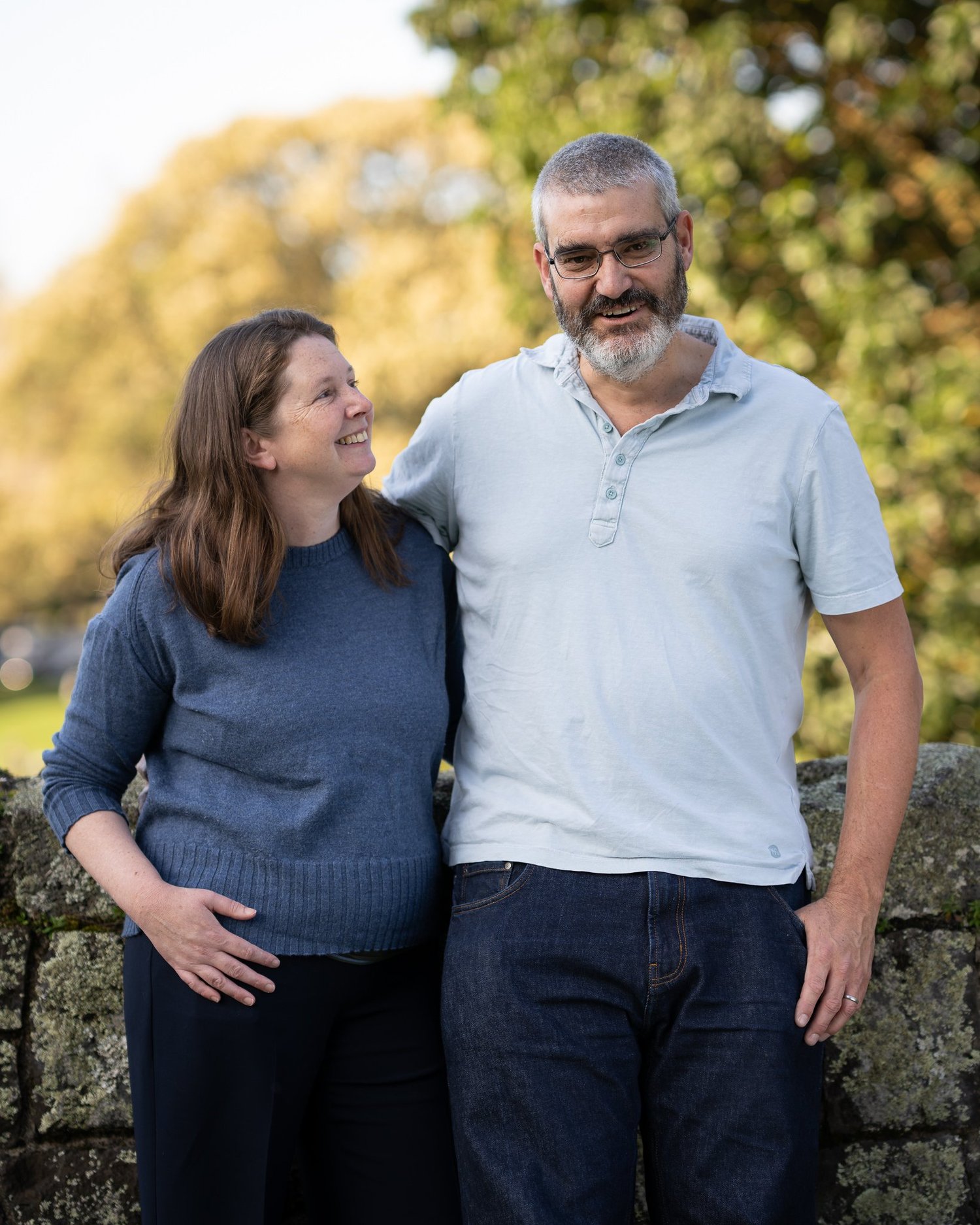 The parents share a smile in front of a stone wall