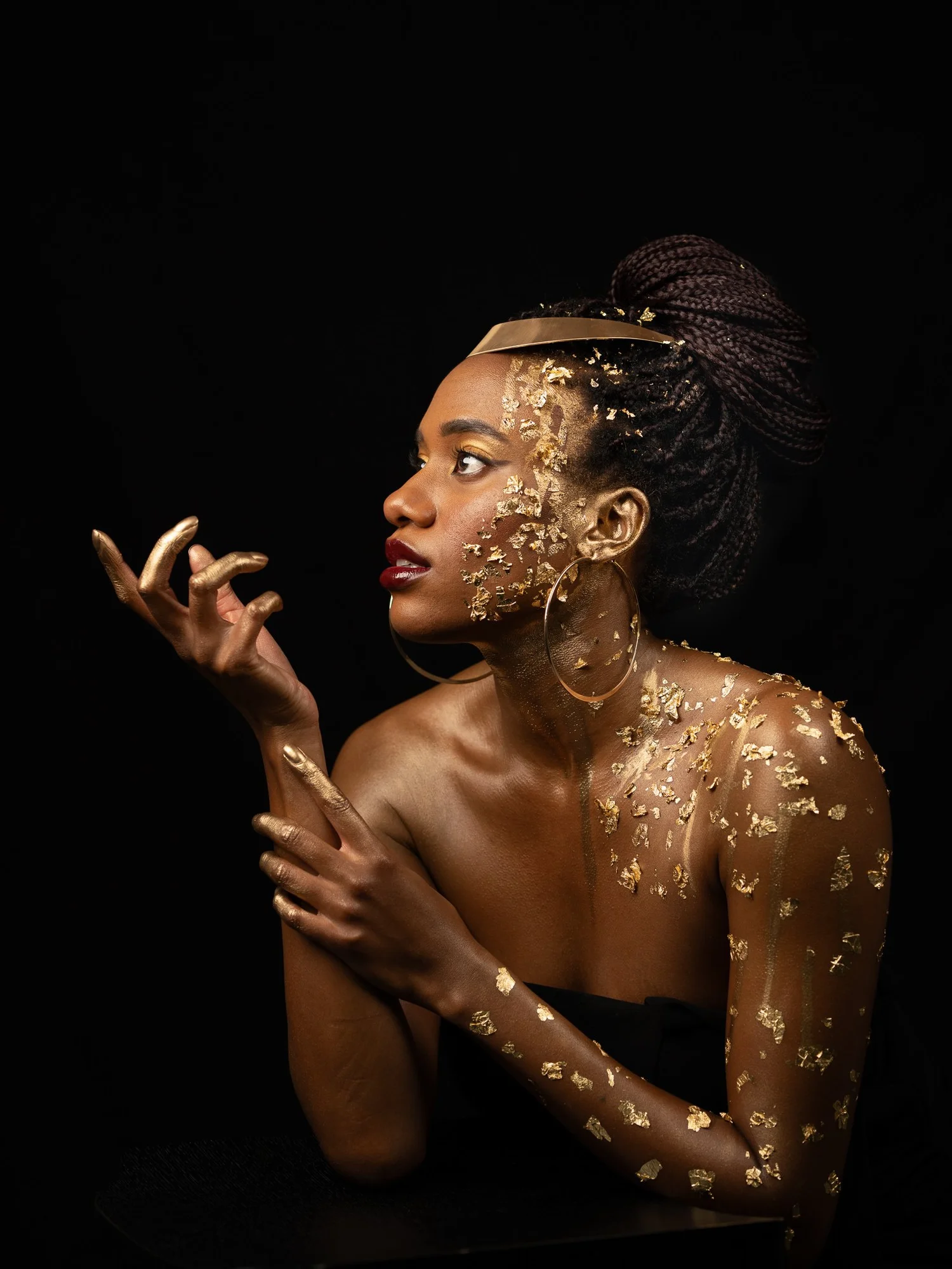 Ty with gold leaf on her skin and a gold headband against black