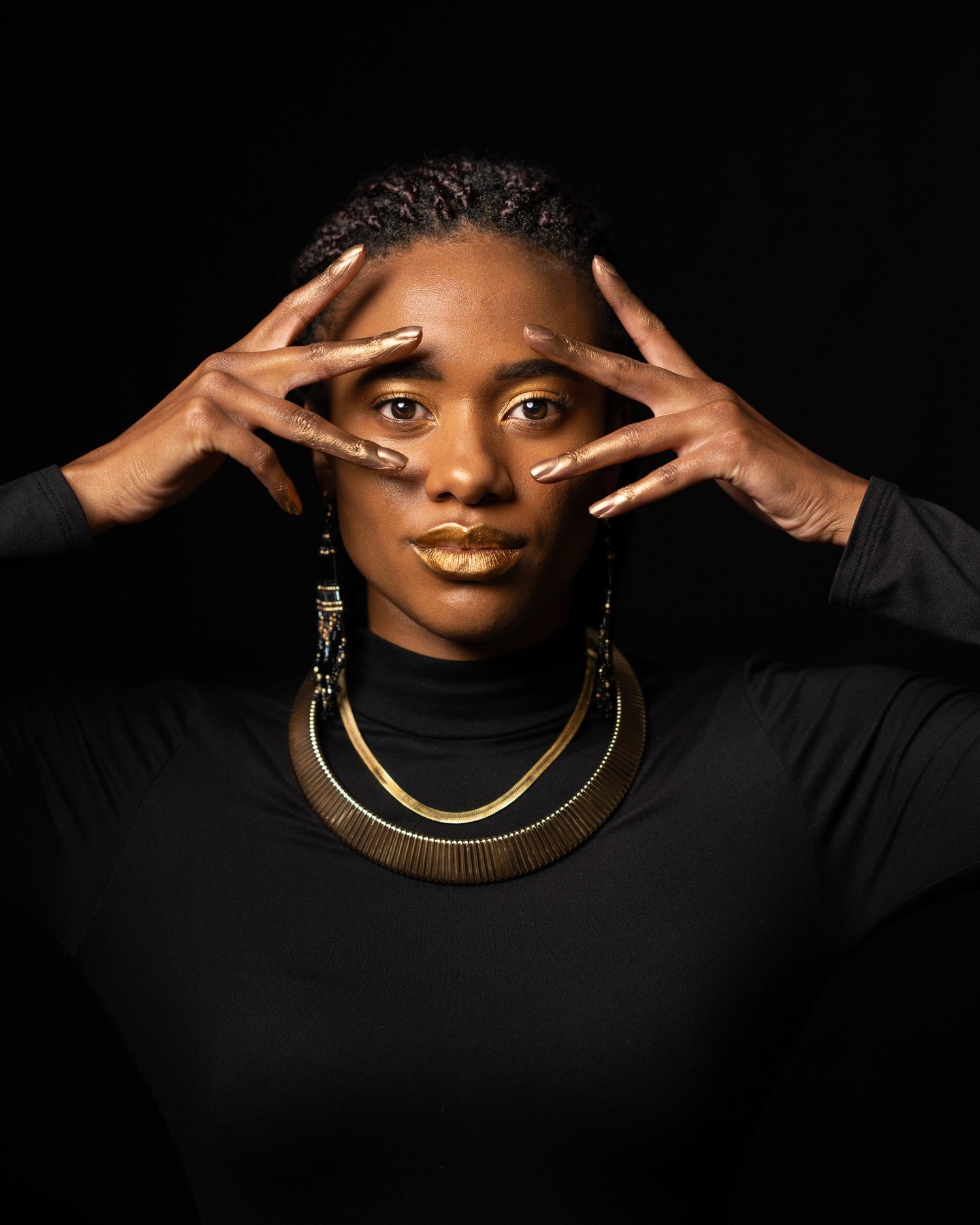 Ty frames her face with her hands in a gold collar