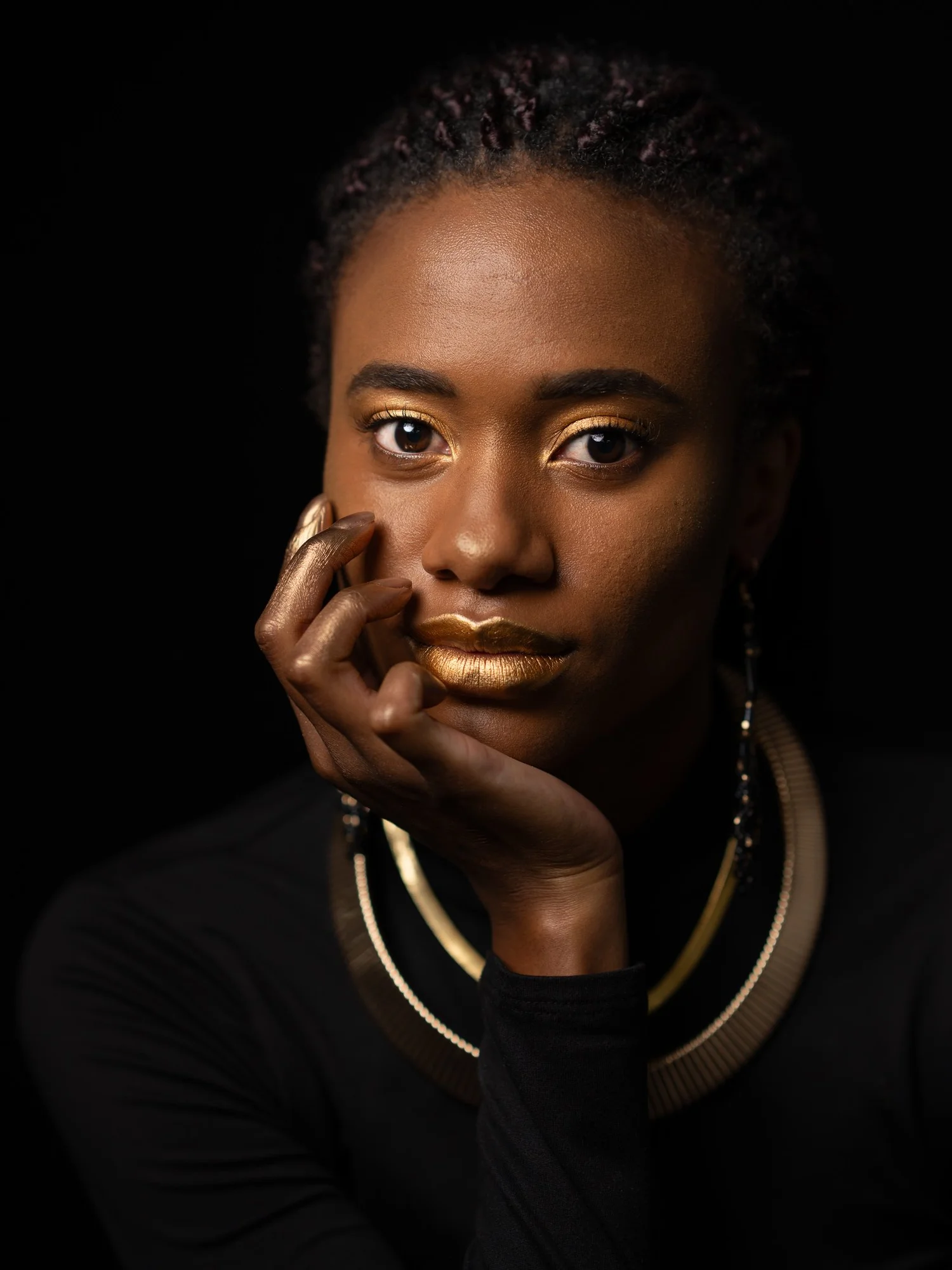 Ty rests her face on her hand in a gold collar and gold lips