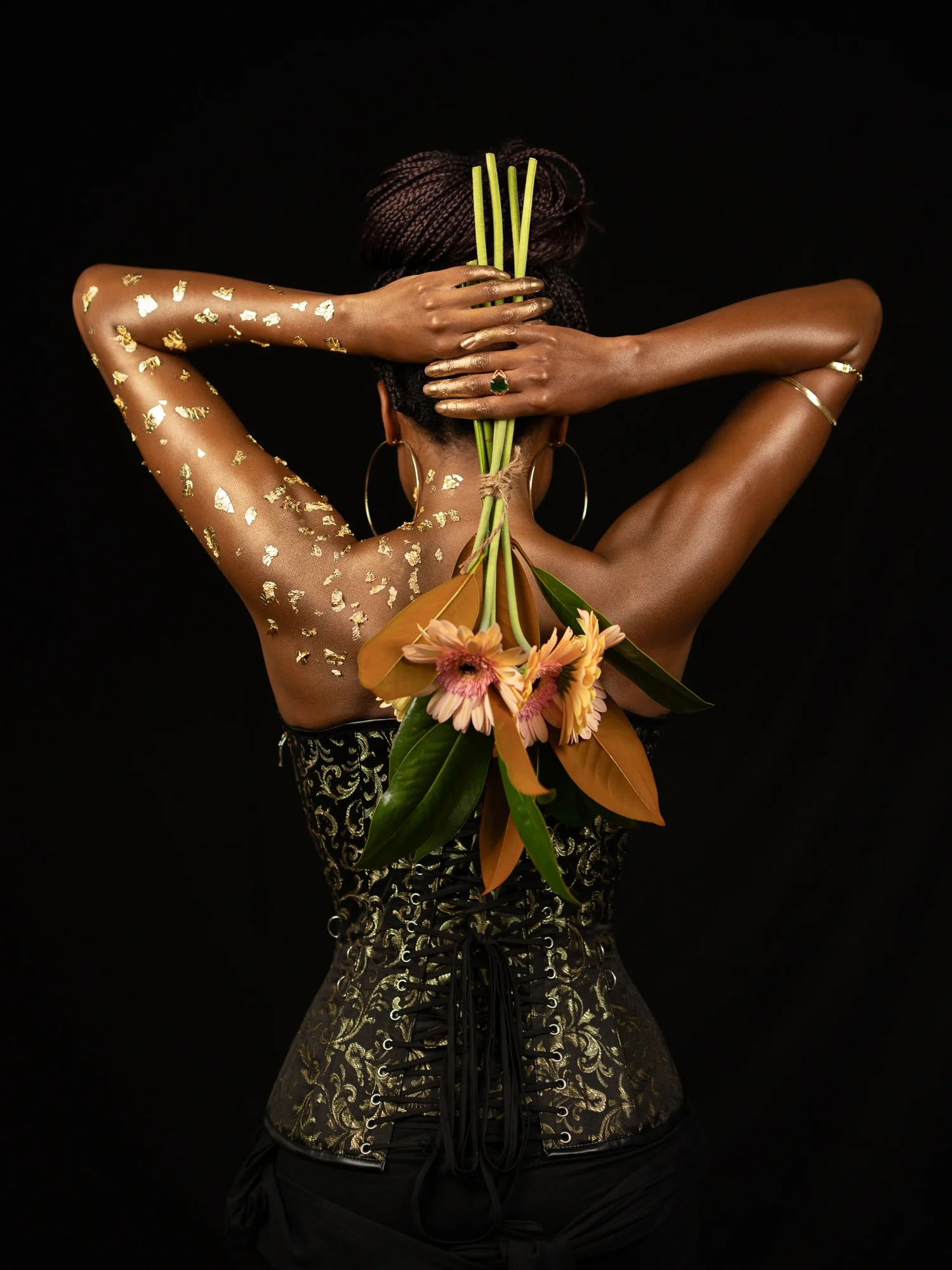 Ty from behind holding orange lilies, her arms dusted with gold
