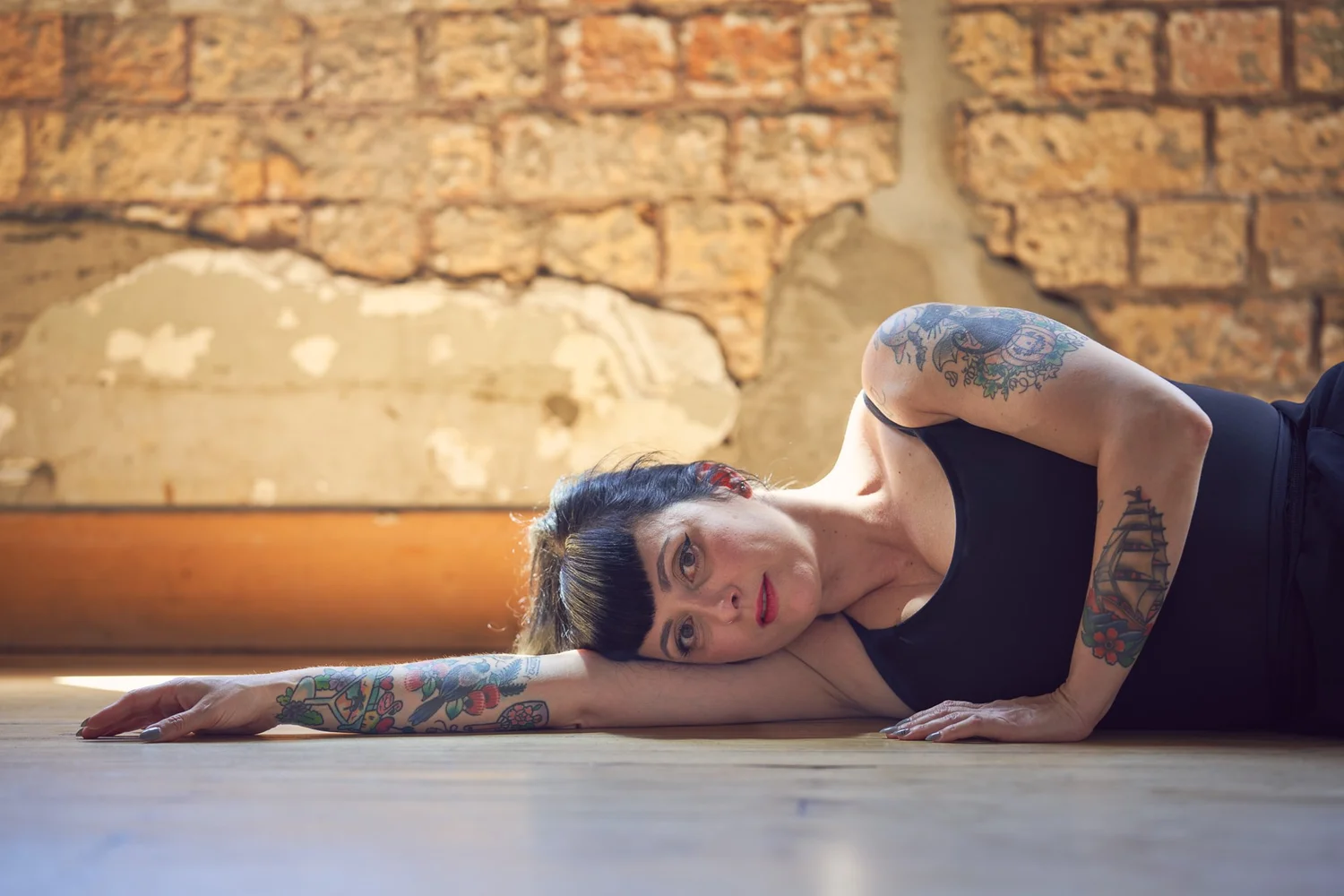 Viv lies on a timber floor showing her tattooed arms