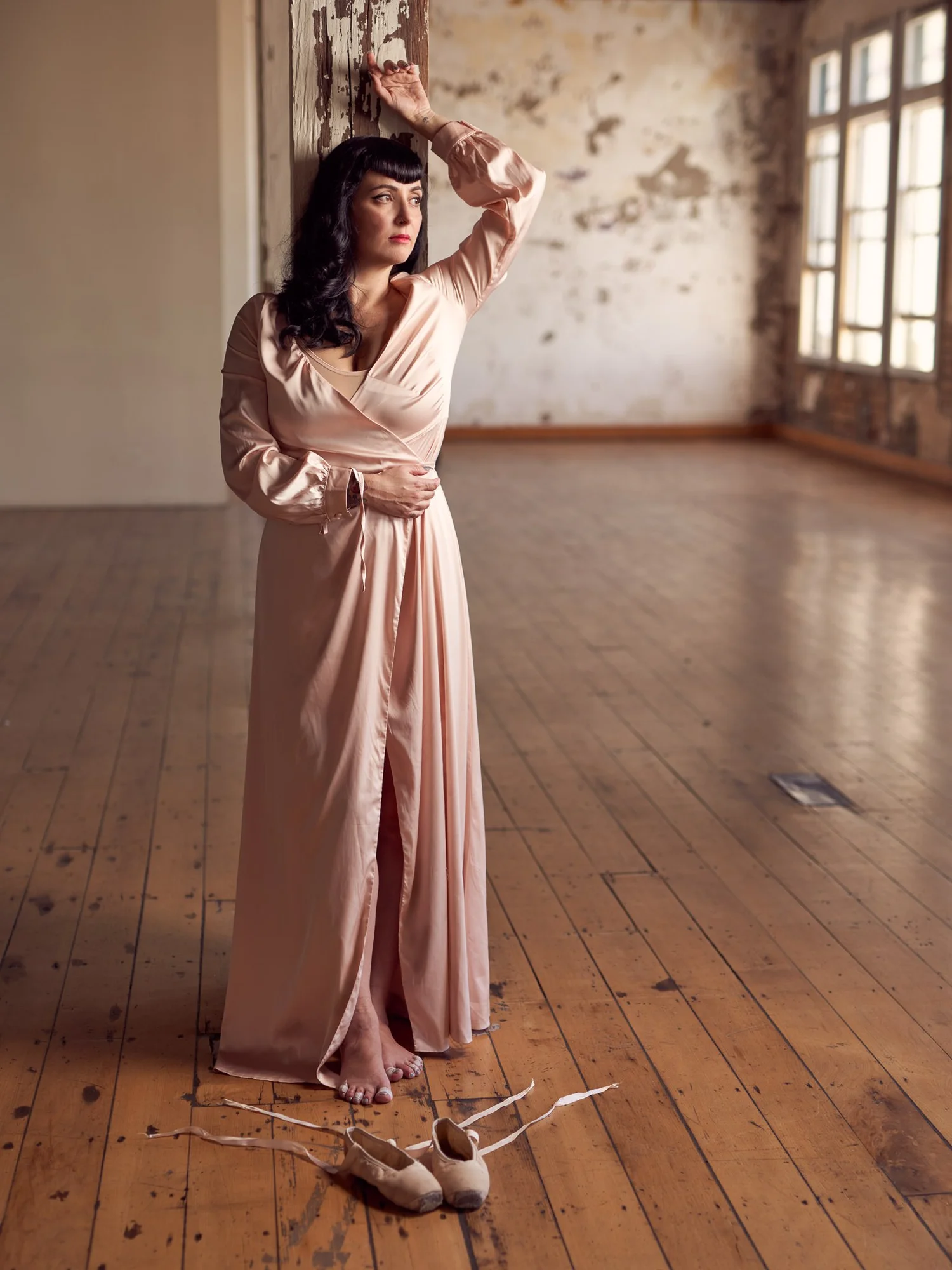 Viv in a long satin gown in an empty room with tall windows