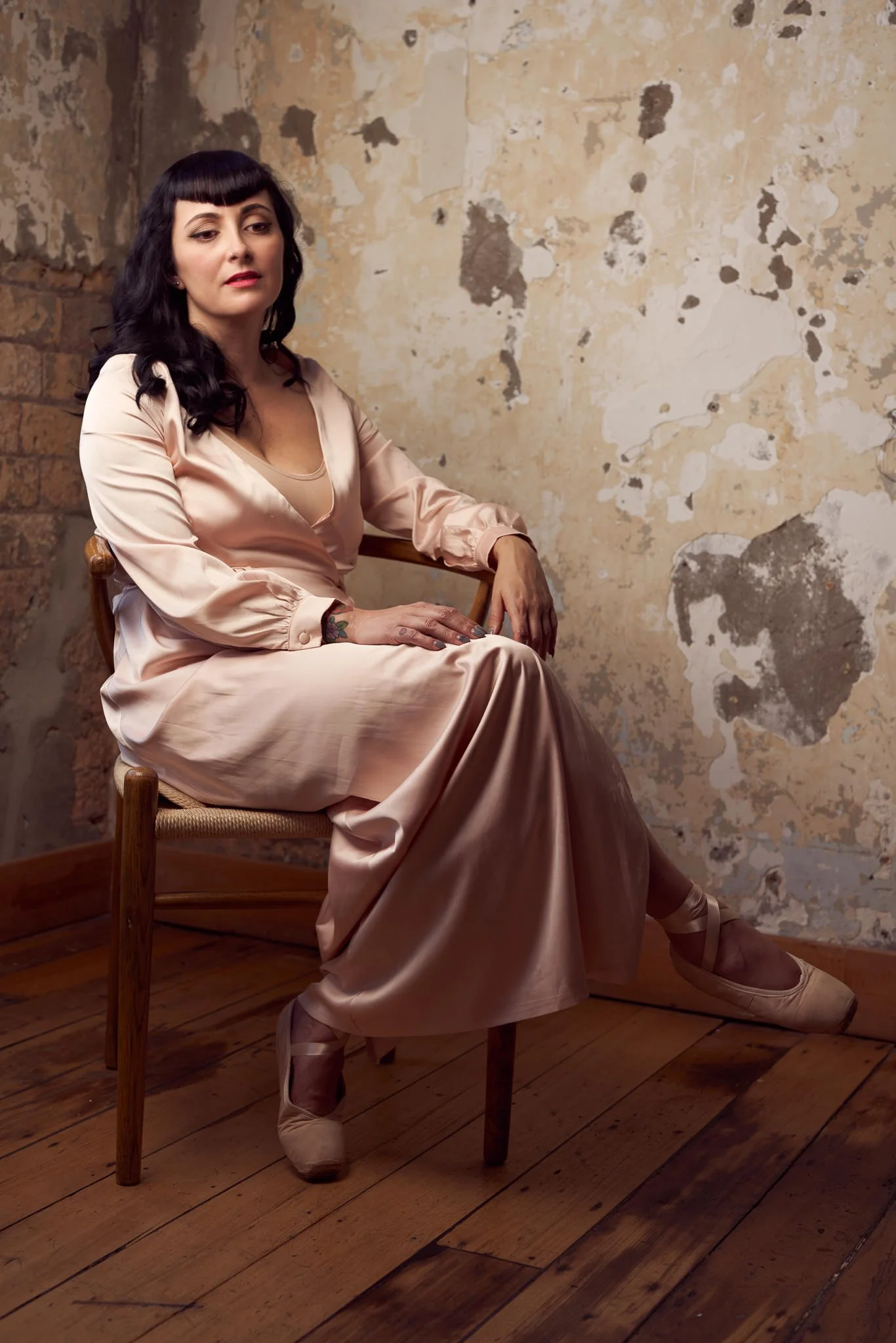 Viv seated in blush satin beside the old wall
