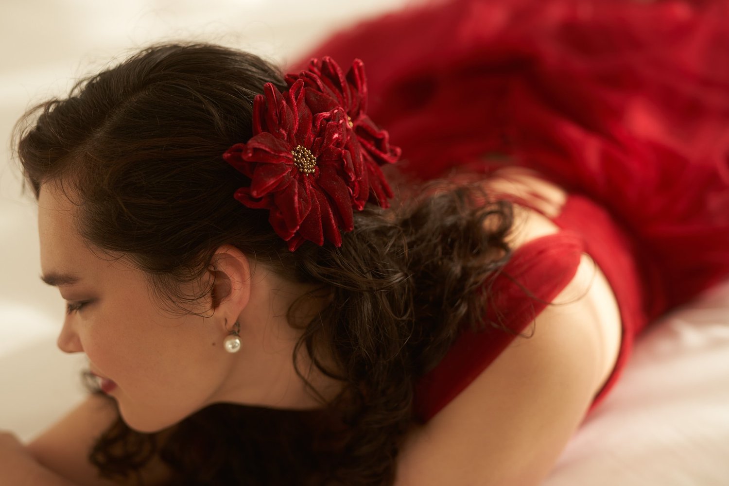 Anita with a red flower in her hair, lying on a bed and looking away