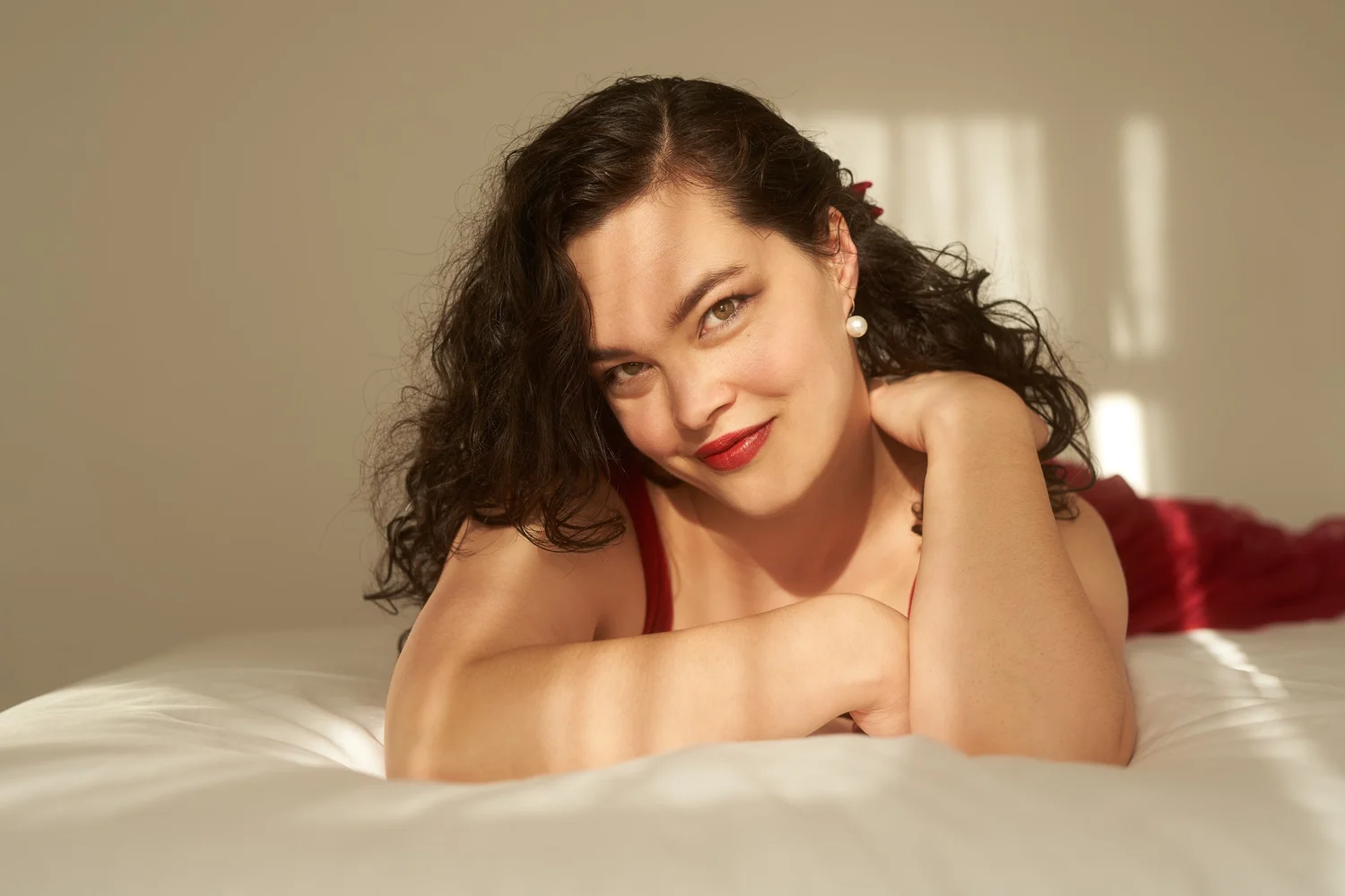 Anita smiles while lying on a white bed