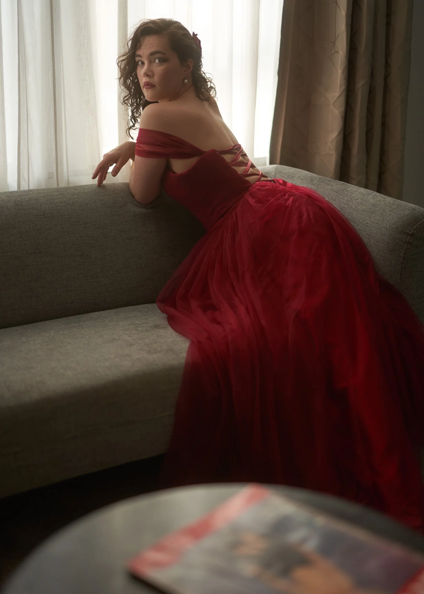 Anita in a red gown leaning over the back of a sofa
