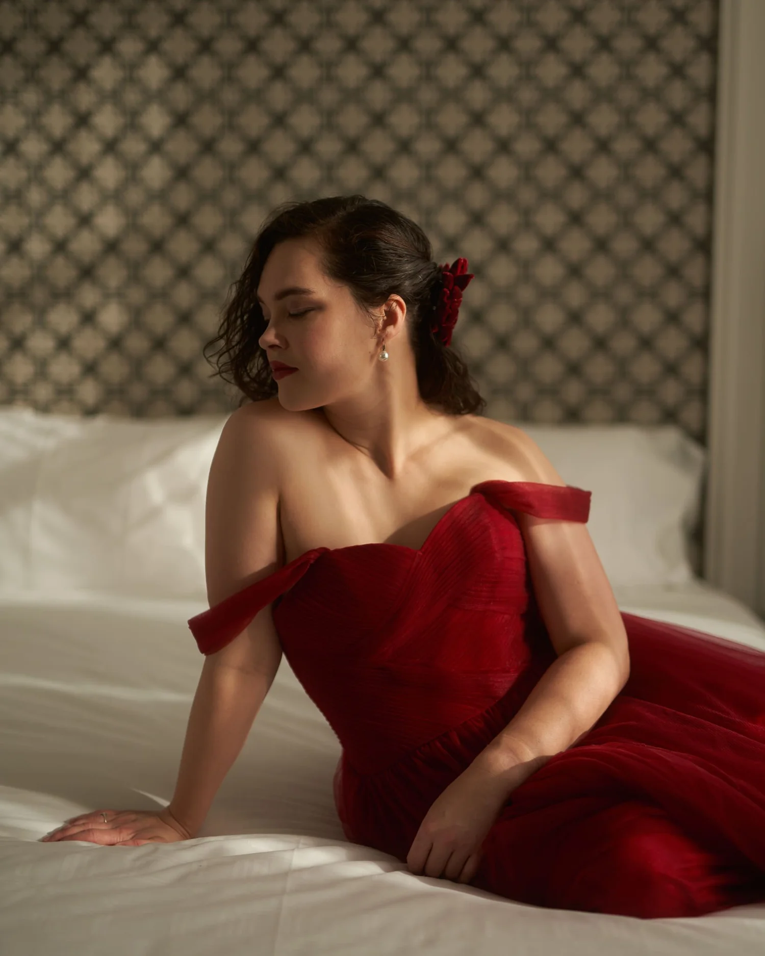 Anita in an off-the-shoulder red gown sitting on the bed