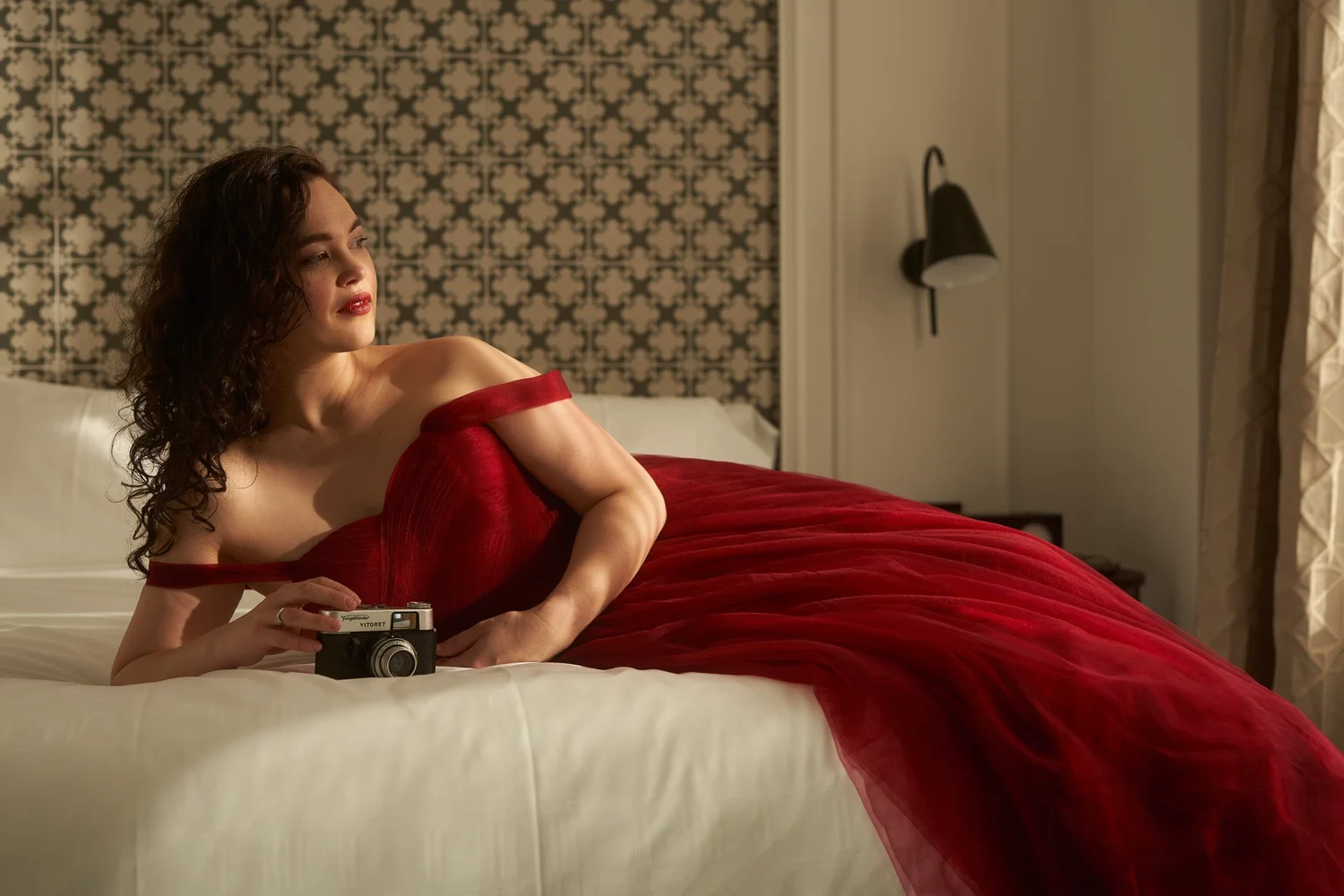 Anita reclines on the bed in her red gown