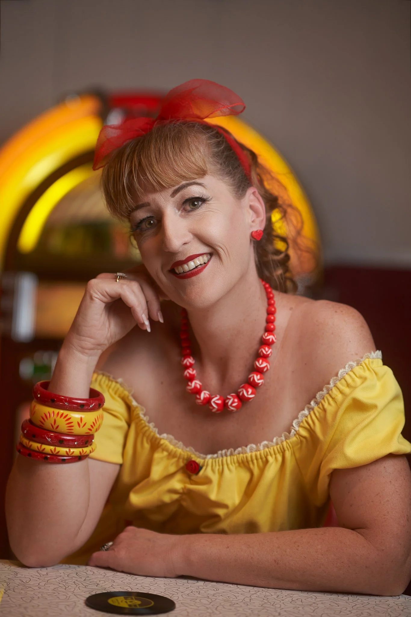Sandy smiles at the counter with a lit jukebox behind