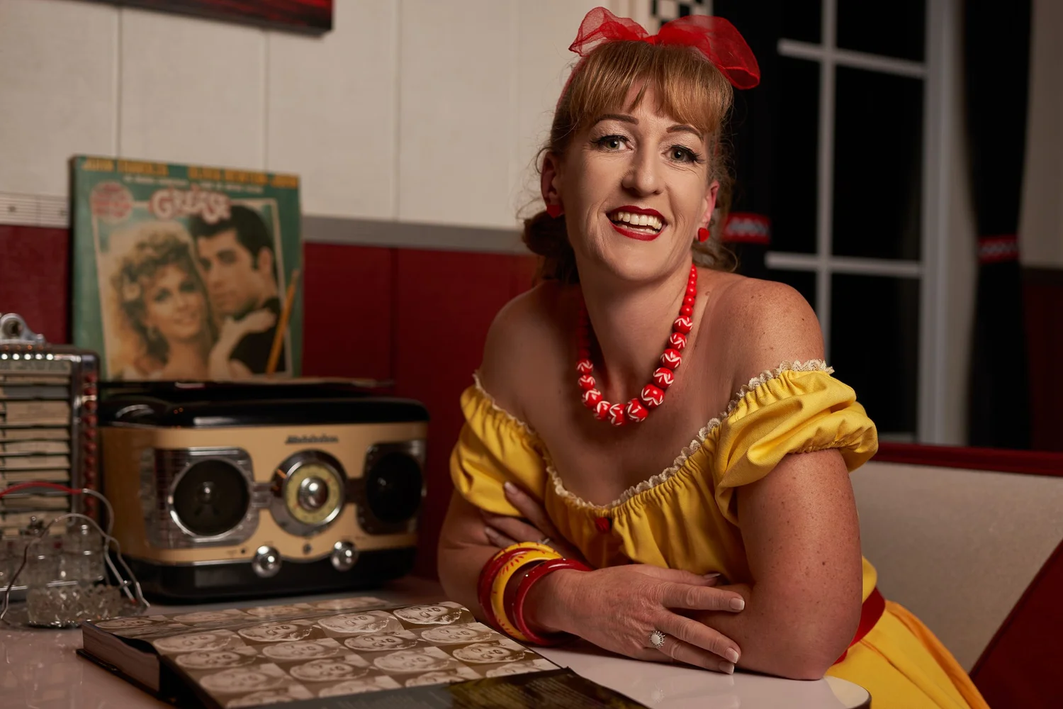Sandy smiles in a diner booth beside a record player