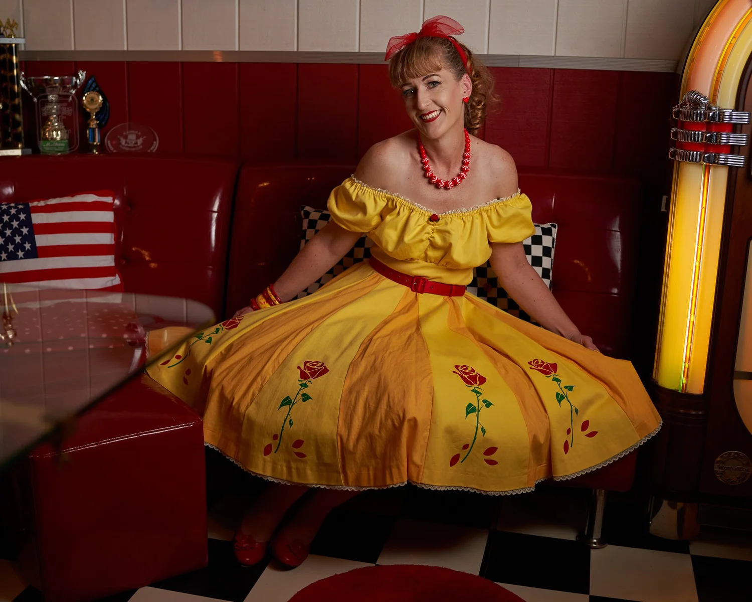 Sandy sits in a red diner booth with her yellow skirt spread out