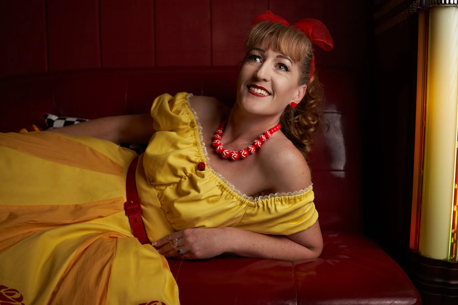 Sandy lies back on the red booth smiling